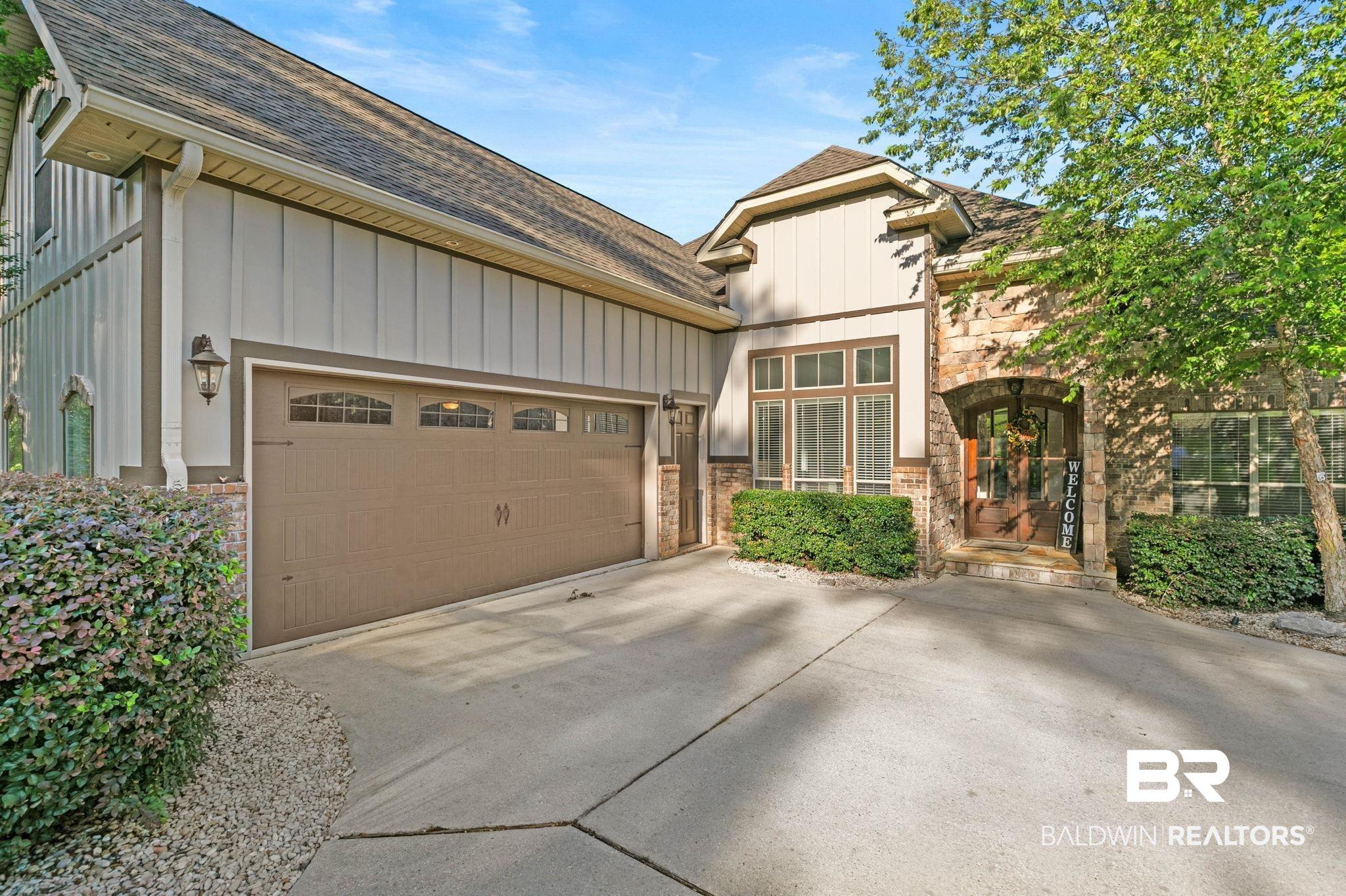 Image 2: Exterior featuring a stone facade, board and batten siding, multiple windows with natural light, an arched entryway, and a two-car garage with transom windows