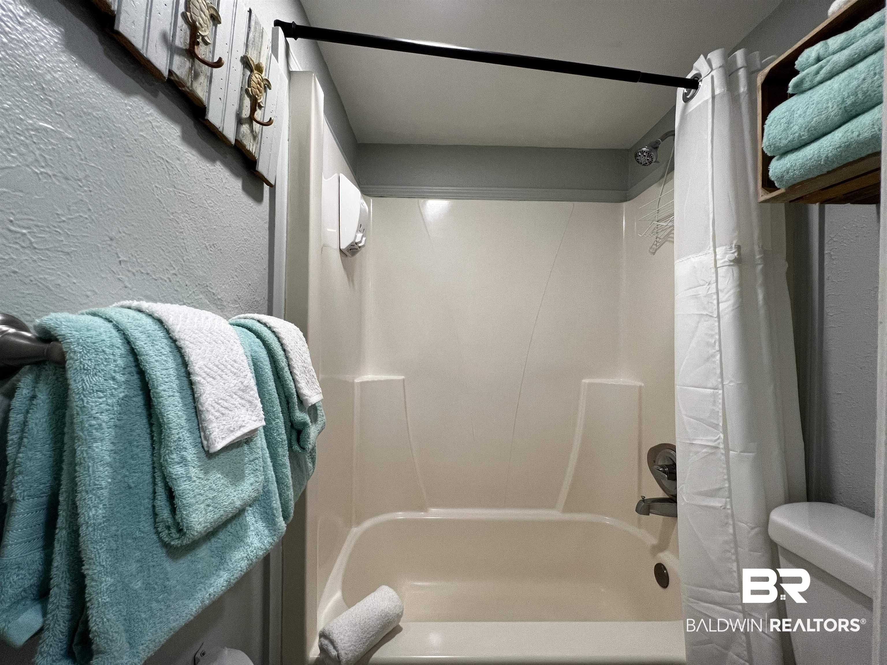 Image 3: Bathroom with a textured wall and shower / bathtub combination with curtain