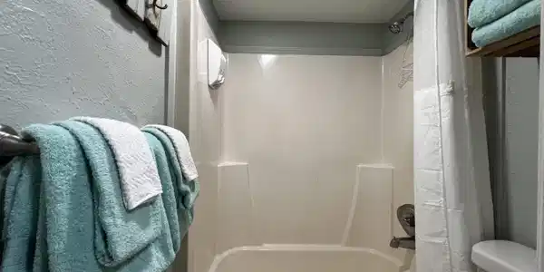 Image 3: Bathroom with a textured wall and shower / bathtub combination with curtain