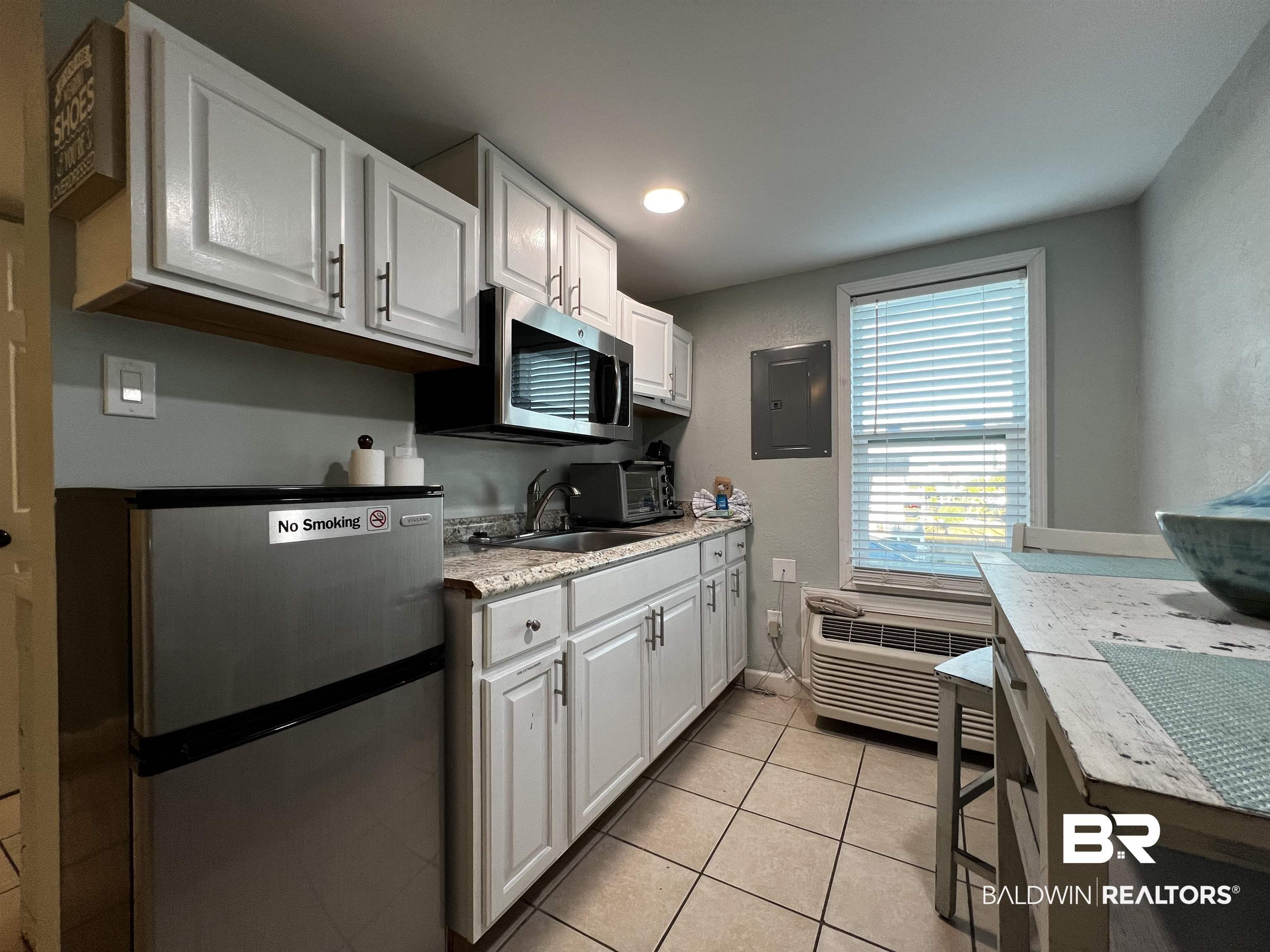 Image 4: Kitchen with stainless steel appliances, white cabinets, electric panel, light tile patterned floors, and light stone countertops