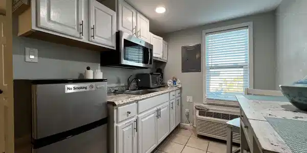 Image 4: Kitchen with stainless steel appliances, white cabinets, electric panel, light tile patterned floors, and light stone countertops