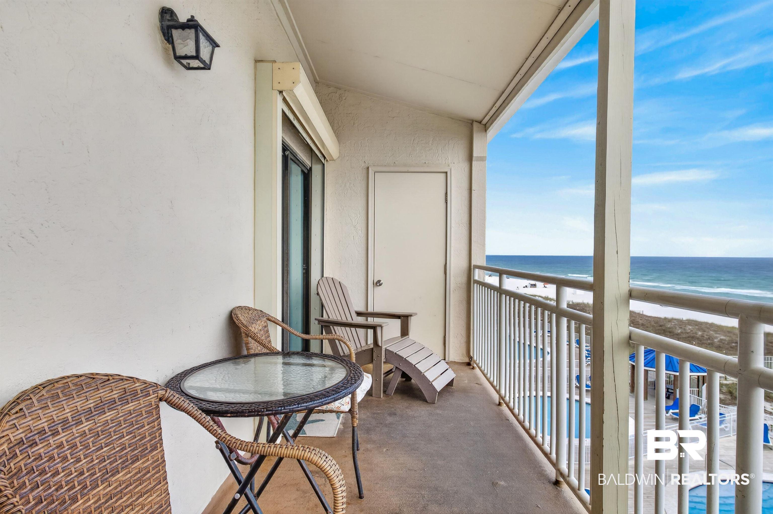 Image 2: Expansive balcony featuring a stucco exterior, sliding glass door access, exterior lantern lighting, and a metal railing overlooking the water