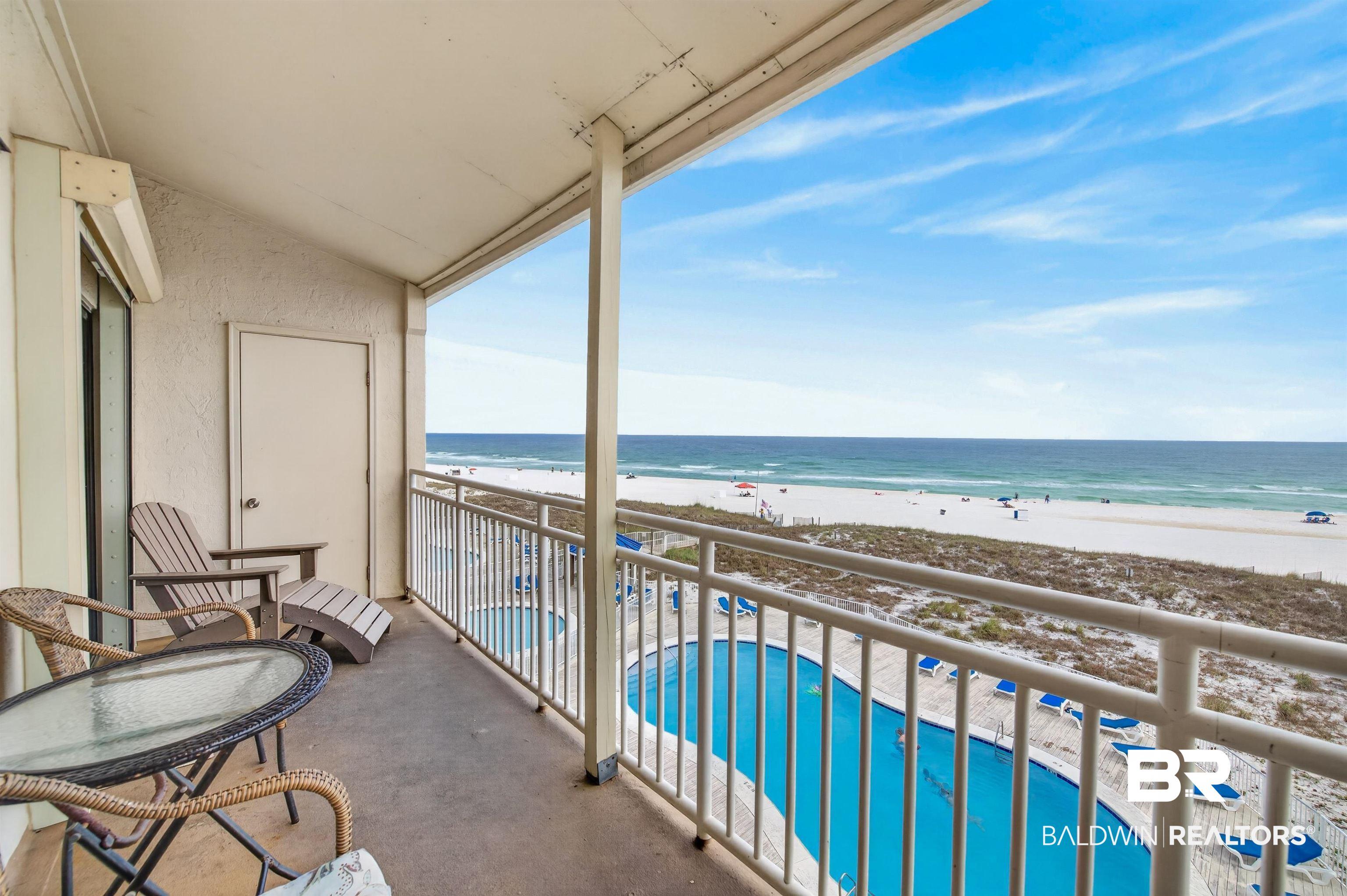 Image 4: Private balcony overlooking a large outdoor swimming pool, white sand beach, and the expanse of the ocean