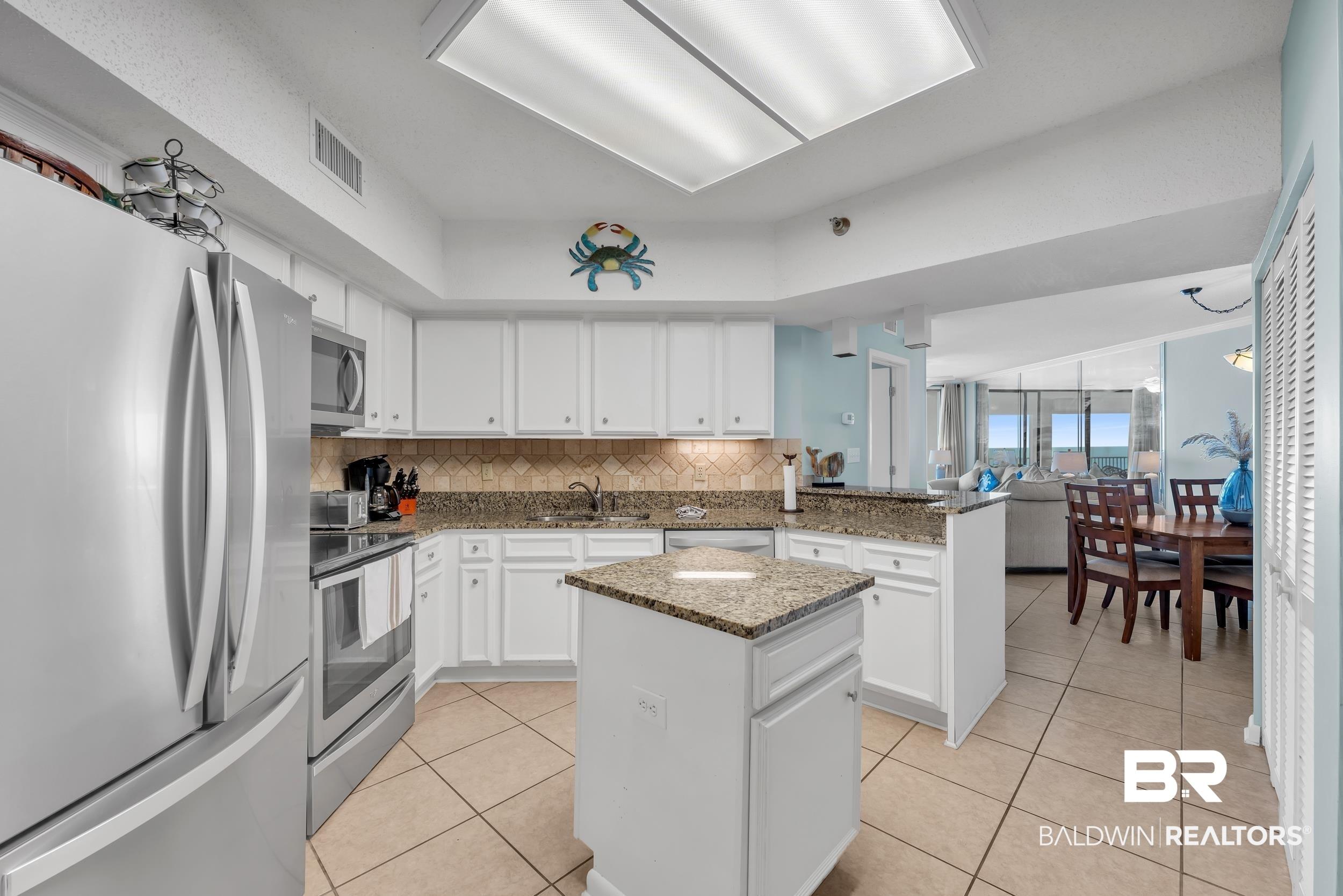 Image 2: Kitchen with backsplash, appliances with stainless steel finishes, light tile patterned flooring, a peninsula, and a center island
