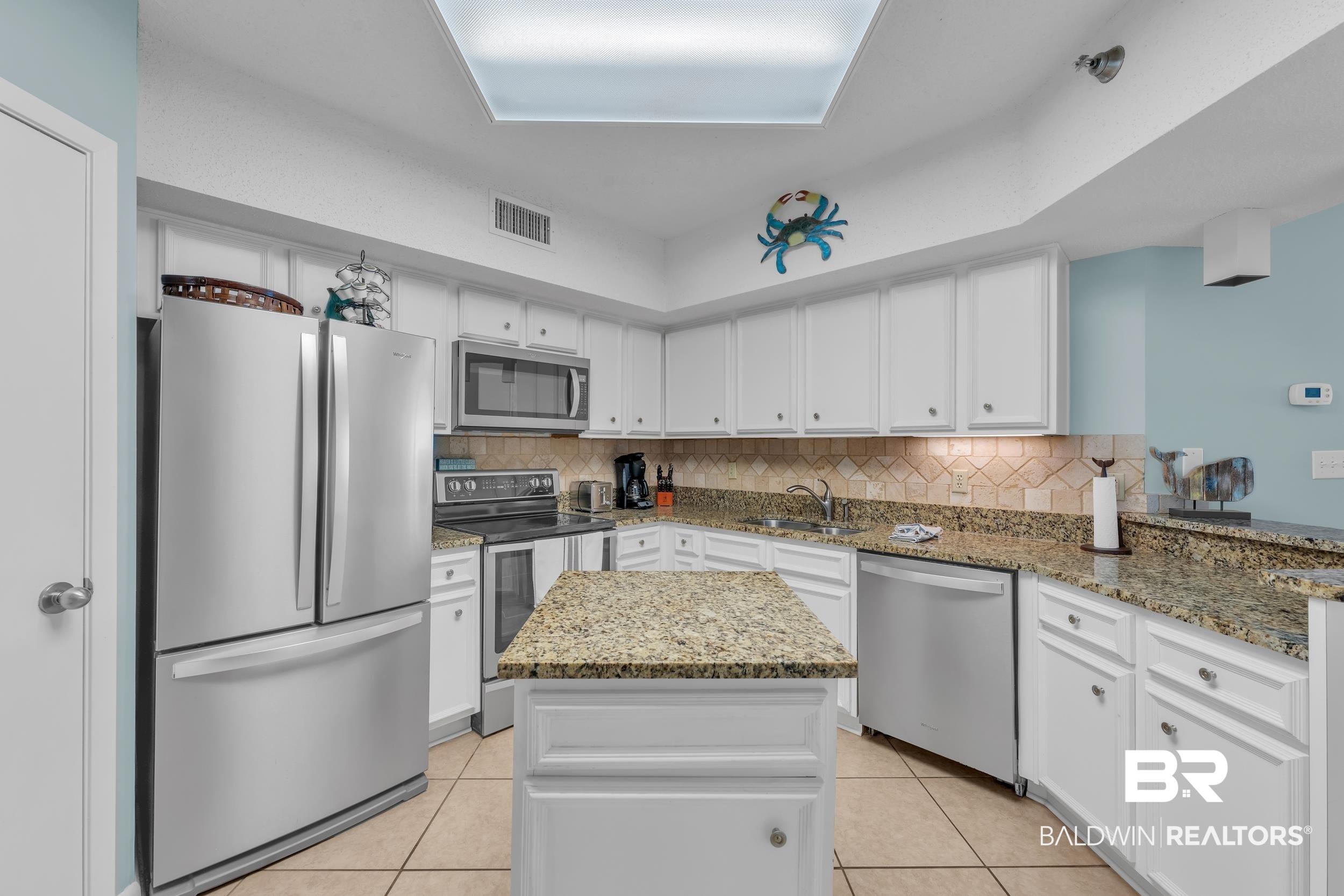 Image 3: Kitchen with appliances with stainless steel finishes, light tile patterned floors, tasteful backsplash, and white cabinetry