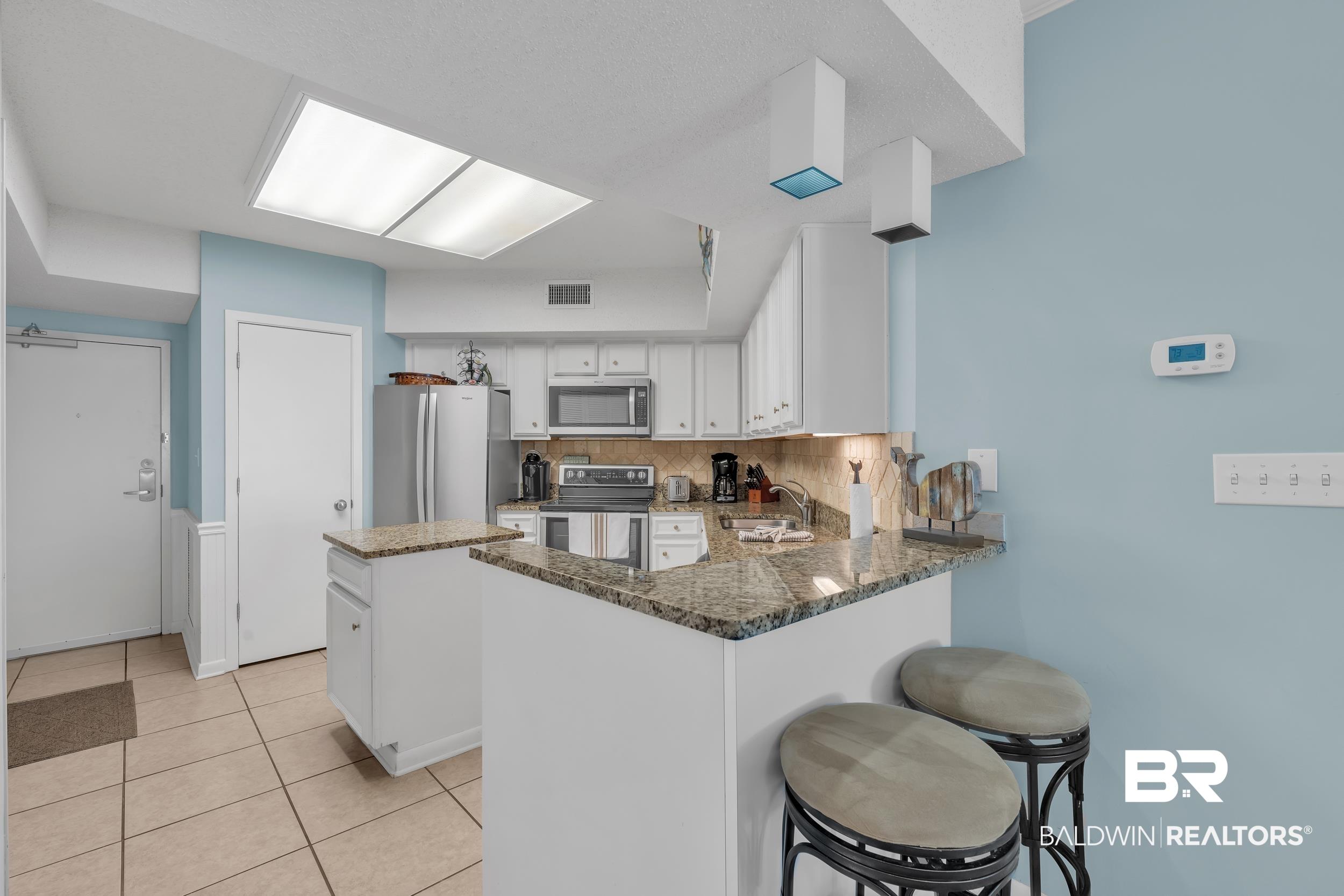 Image 4: Kitchen with backsplash, a peninsula, stainless steel appliances, dark stone countertops, and white cabinets