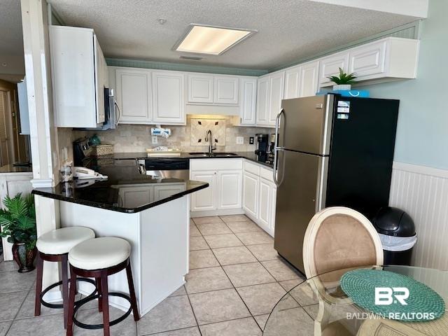 Image 4: Kitchen with white cabinets, stainless steel appliances, a peninsula, dark stone counters, and a kitchen breakfast bar