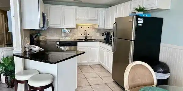Image 4: Kitchen with white cabinets, stainless steel appliances, a peninsula, dark stone counters, and a kitchen breakfast bar