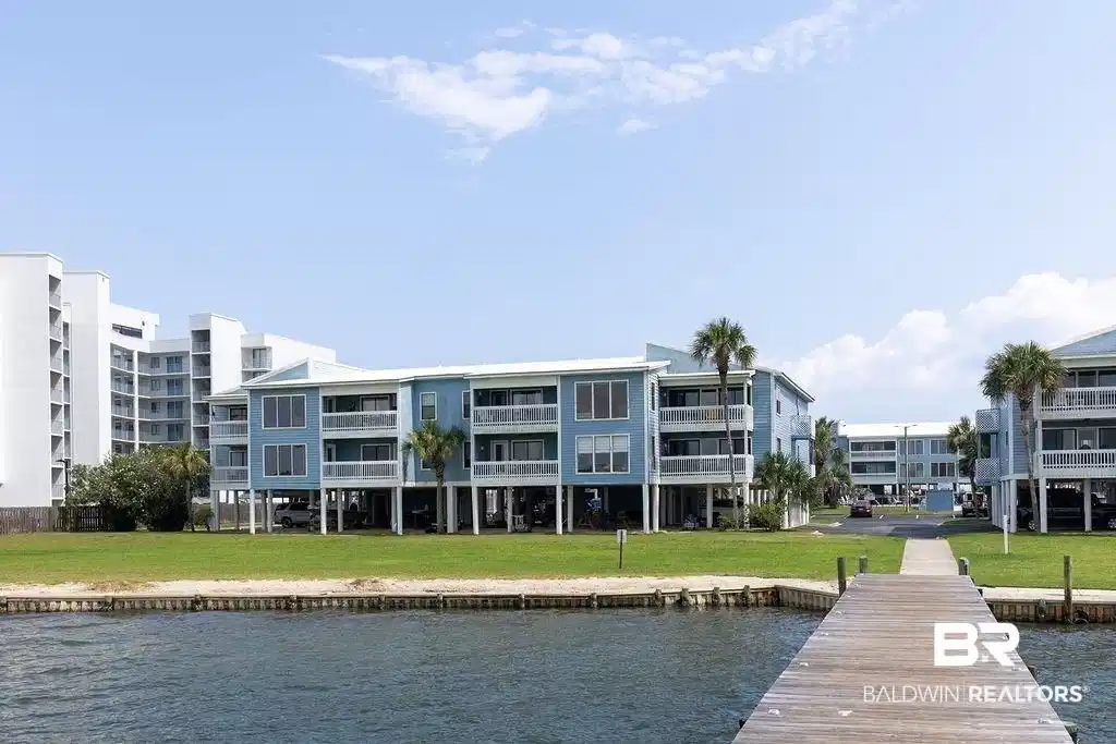 Image 1: Waterfront property featuring a wooden pier, green lawn, and sandy shoreline