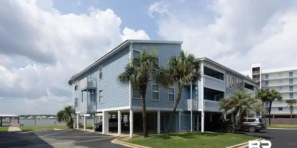Image 2: Multi-story coastal building with light blue siding, multiple balconies, and a ground-level parking area