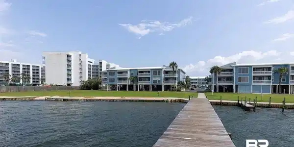 Image 3: Wooden pier extending into a body of water, bordered by a grassy shoreline and coastal buildings