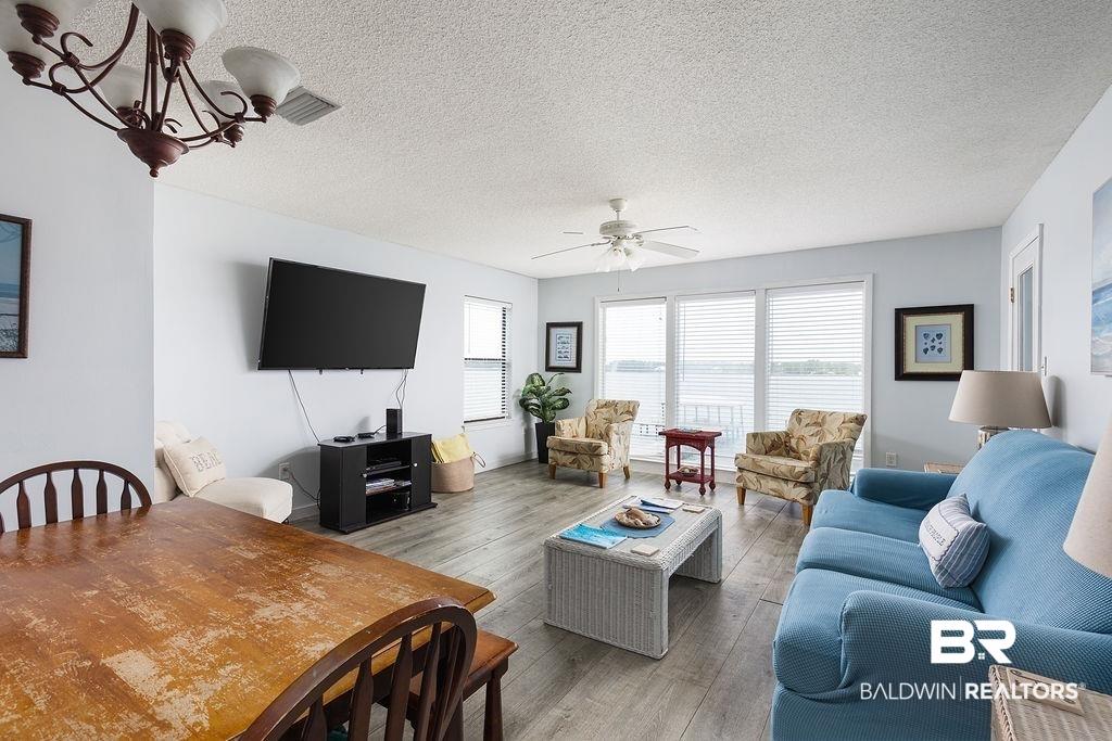 Image 4: Spacious living area featuring wood-finish flooring, a ceiling fan, and sliding glass doors with horizontal blinds