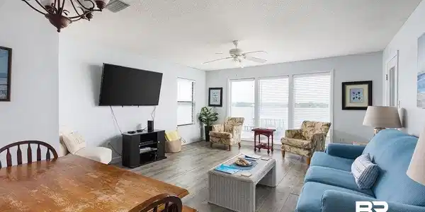 Image 4: Spacious living area featuring wood-finish flooring, a ceiling fan, and sliding glass doors with horizontal blinds