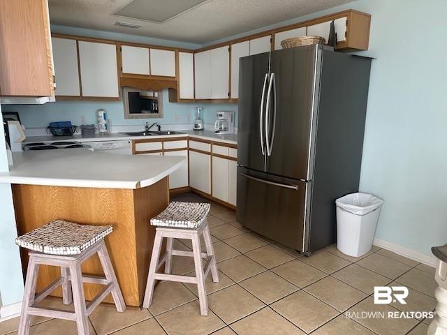 Image 4: Kitchen featuring light countertops, white cabinets, a kitchen bar, freestanding refrigerator, and a peninsula