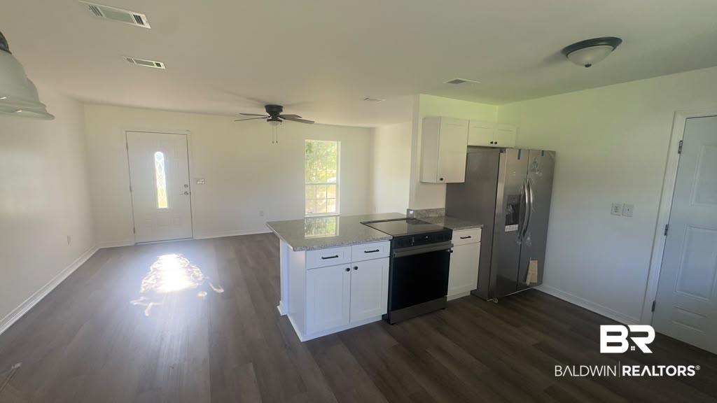 Image 2: Open-concept living space with wood-finish flooring, a kitchen island with stone-finish countertop, white cabinetry, and stainless steel appliances