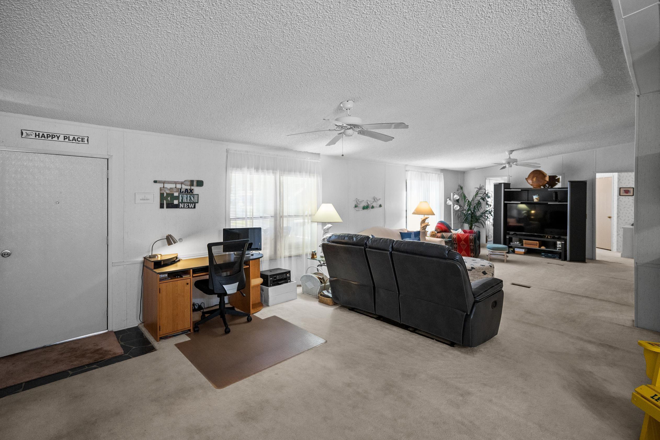 Image 4: Carpeted living area with ceiling fan, a desk, and a textured ceiling