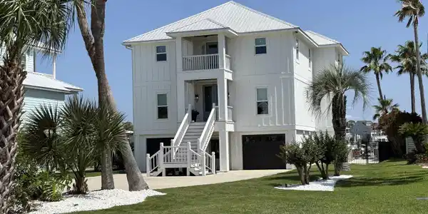 Image 2: White exterior with vertical siding and a metal roof