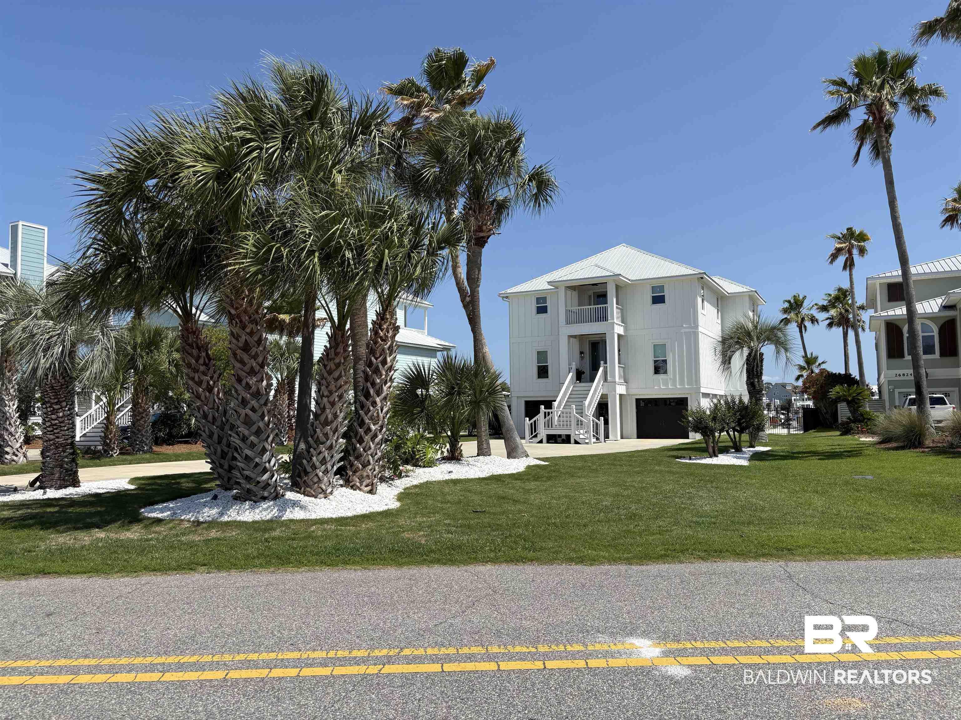 Image 3: Stilted white residence featuring a metal roof, multiple balconies, a ground-level garage, and an elevated entrance staircase