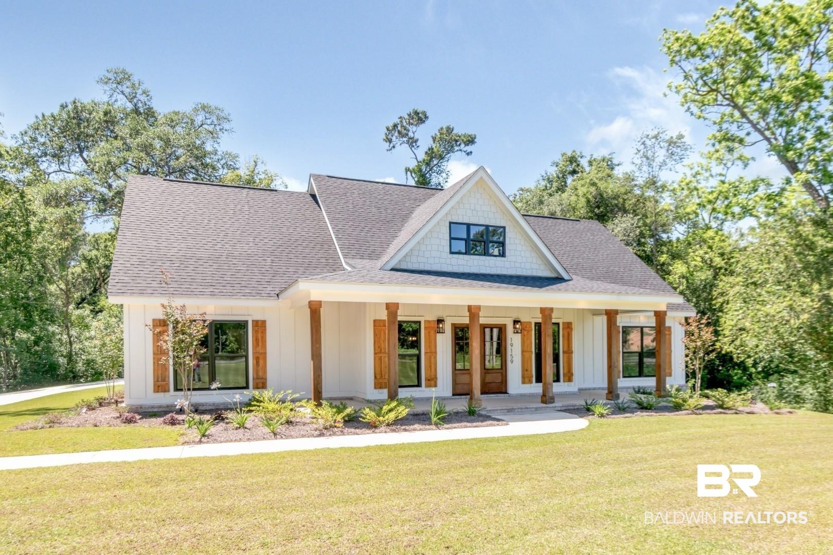 Image 2: Modern farmhouse-style exterior featuring white vertical siding, a dark shingled roof, a covered porch with natural wood columns, and dark-framed windows with decorative wood shutters