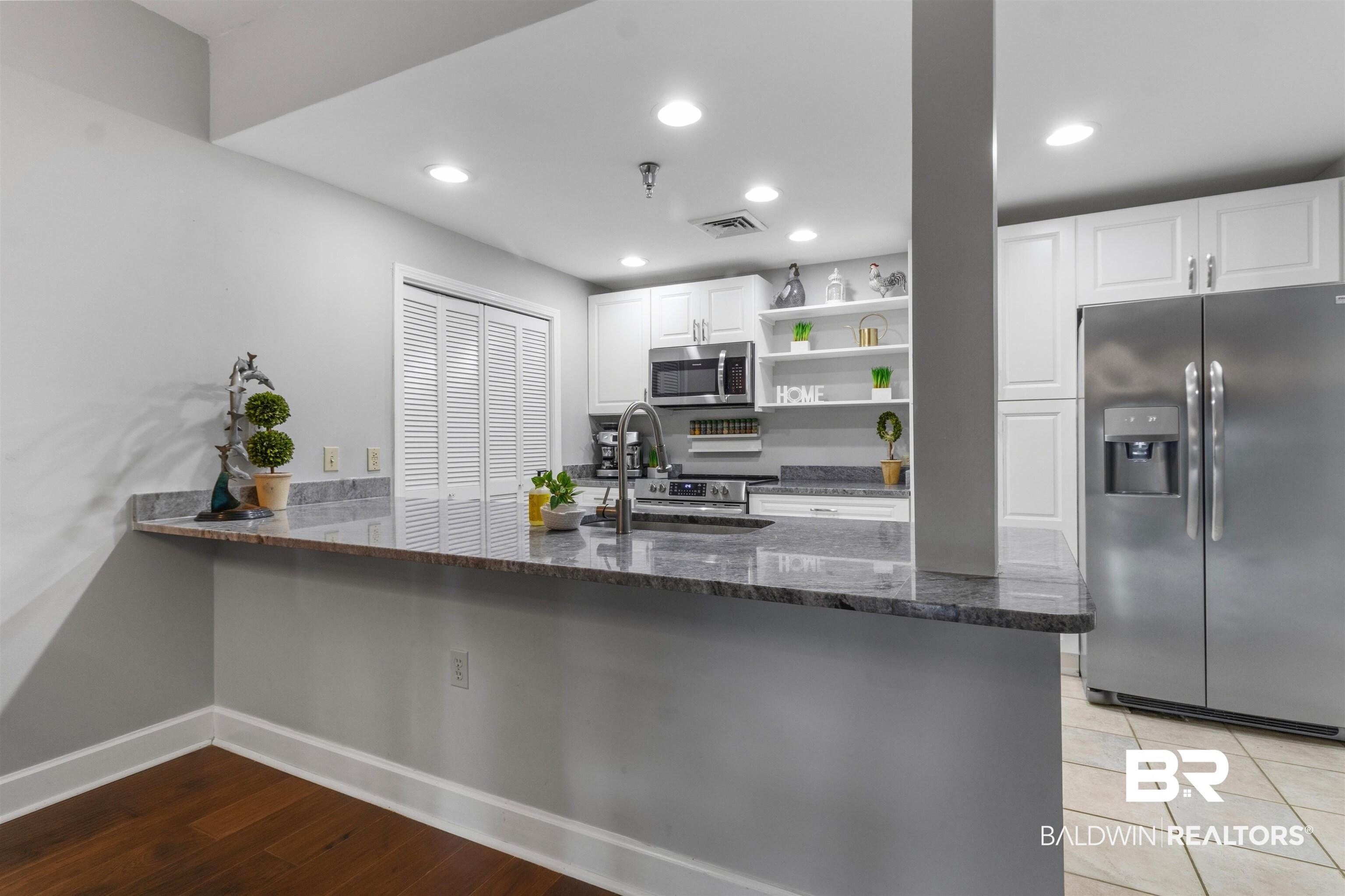 Image 3: Kitchen featuring a breakfast bar with granite countertops, stainless steel appliances, white cabinetry, and recessed lighting