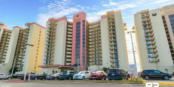 Image 3: Multi-story building featuring individual balconies, a covered porte-cochere entrance, and a parking area