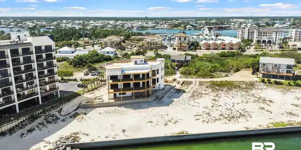 Image 2: Waterfront property featuring a partially constructed multi-story building, sandy ground, a concrete retaining wall, and a rocky shoreline