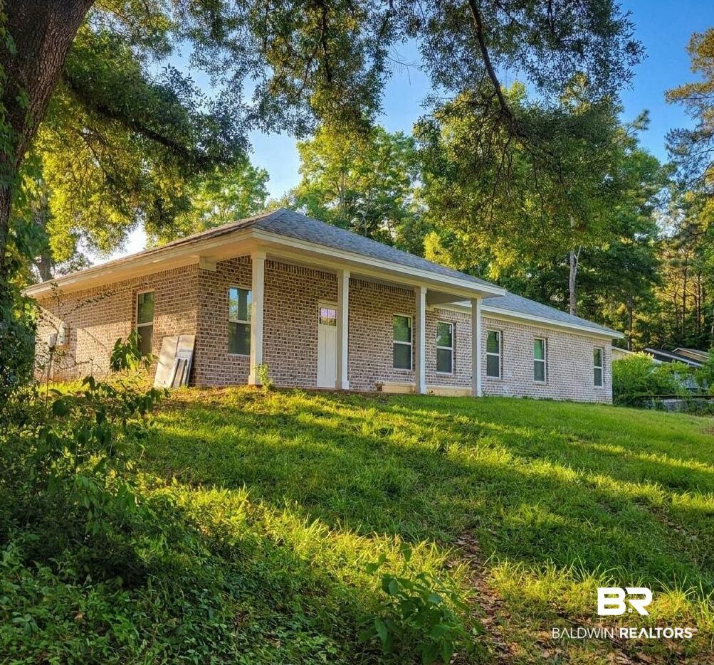 Image 2: Brick exterior home featuring a covered front porch with white columns, multiple windows, and a surrounding natural landscape with mature trees