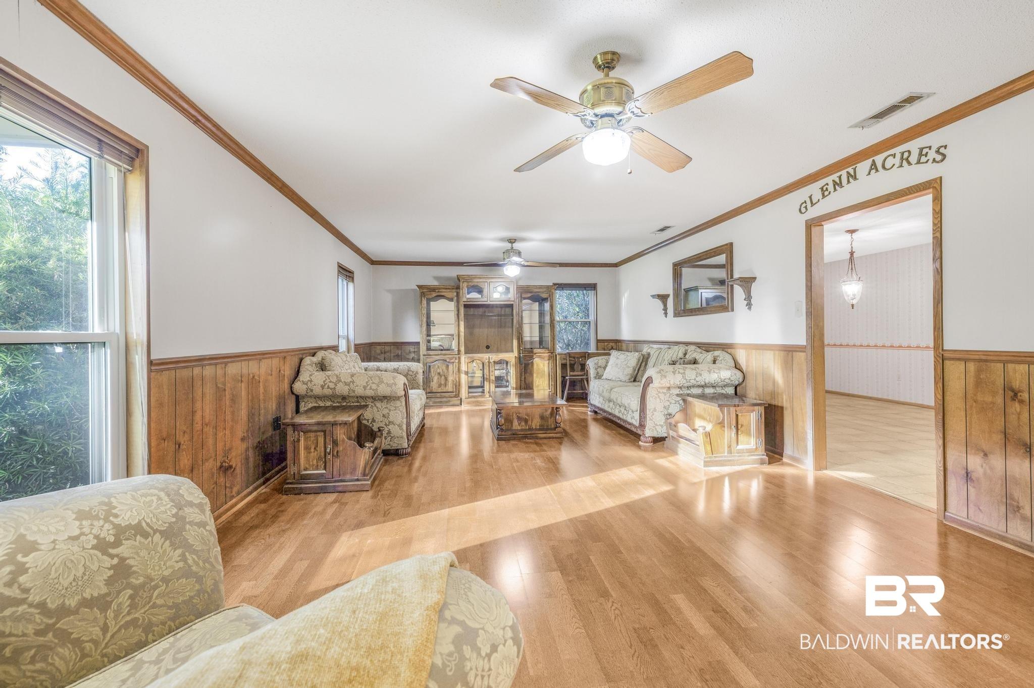 Image 4: Living room featuring wooden walls, a wainscoted wall, light wood-style floors, ornamental molding, and a ceiling fan