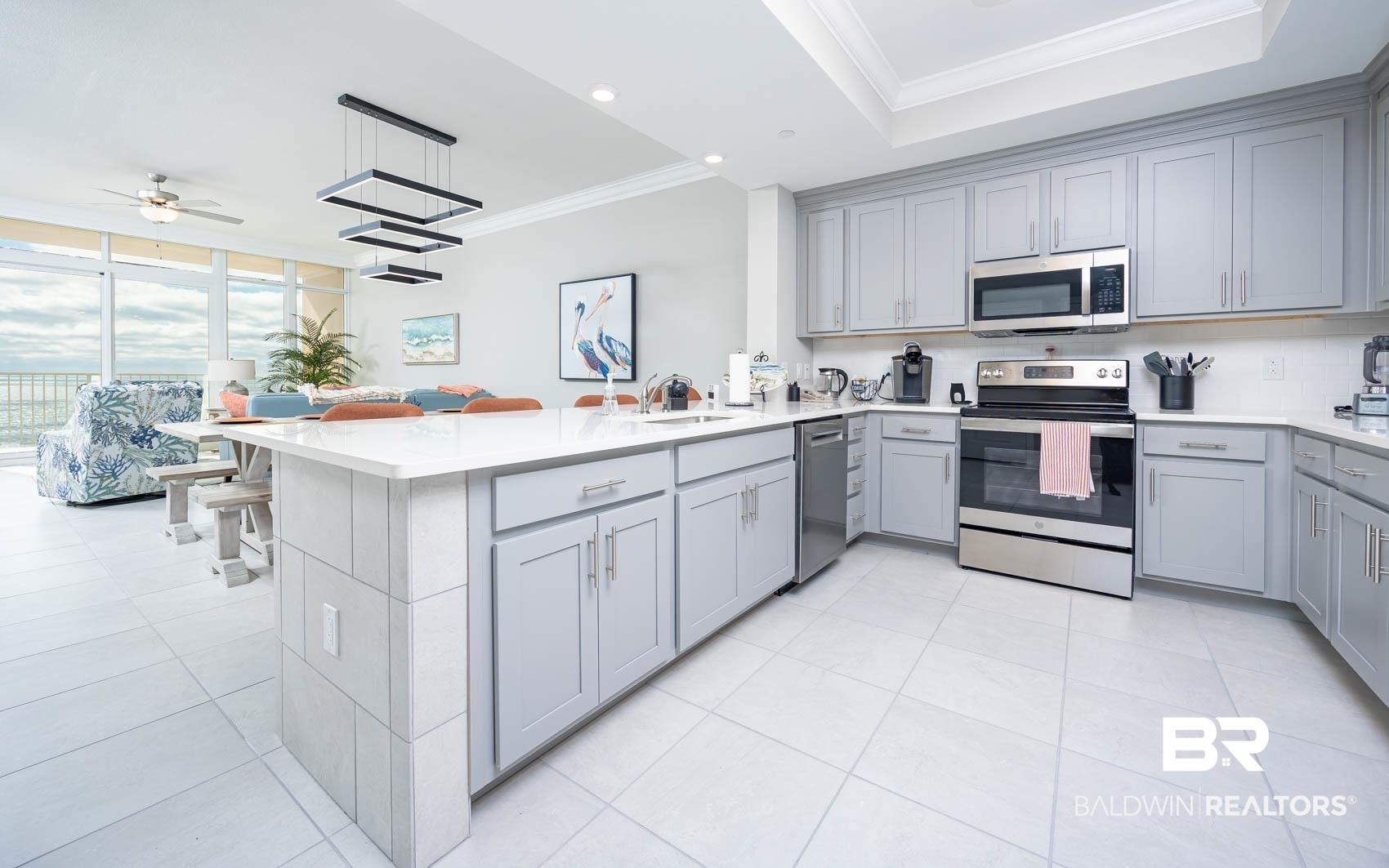 Image 4: Kitchen featuring appliances with stainless steel finishes, gray cabinets, ornamental molding, decorative light fixtures, and a peninsula