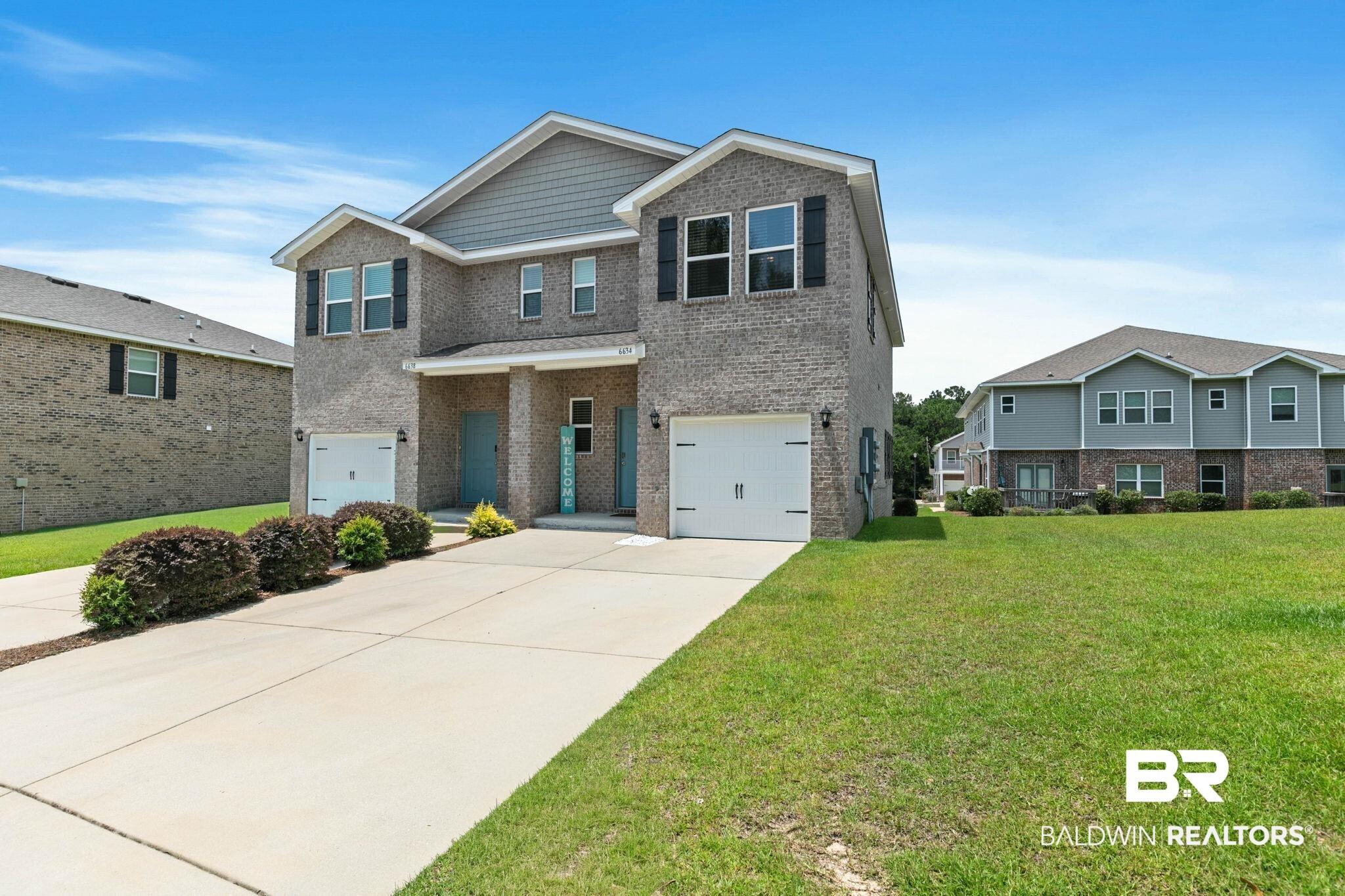 Image 2: Contemporary two-story duplex featuring a brick and siding exterior, individual garages, and separate entryways