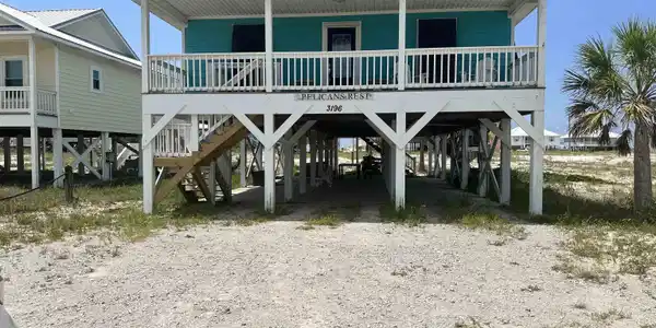 Image 3: Elevated coastal dwelling featuring a vibrant teal exterior, a covered front porch with white railing, and a durable metal roof