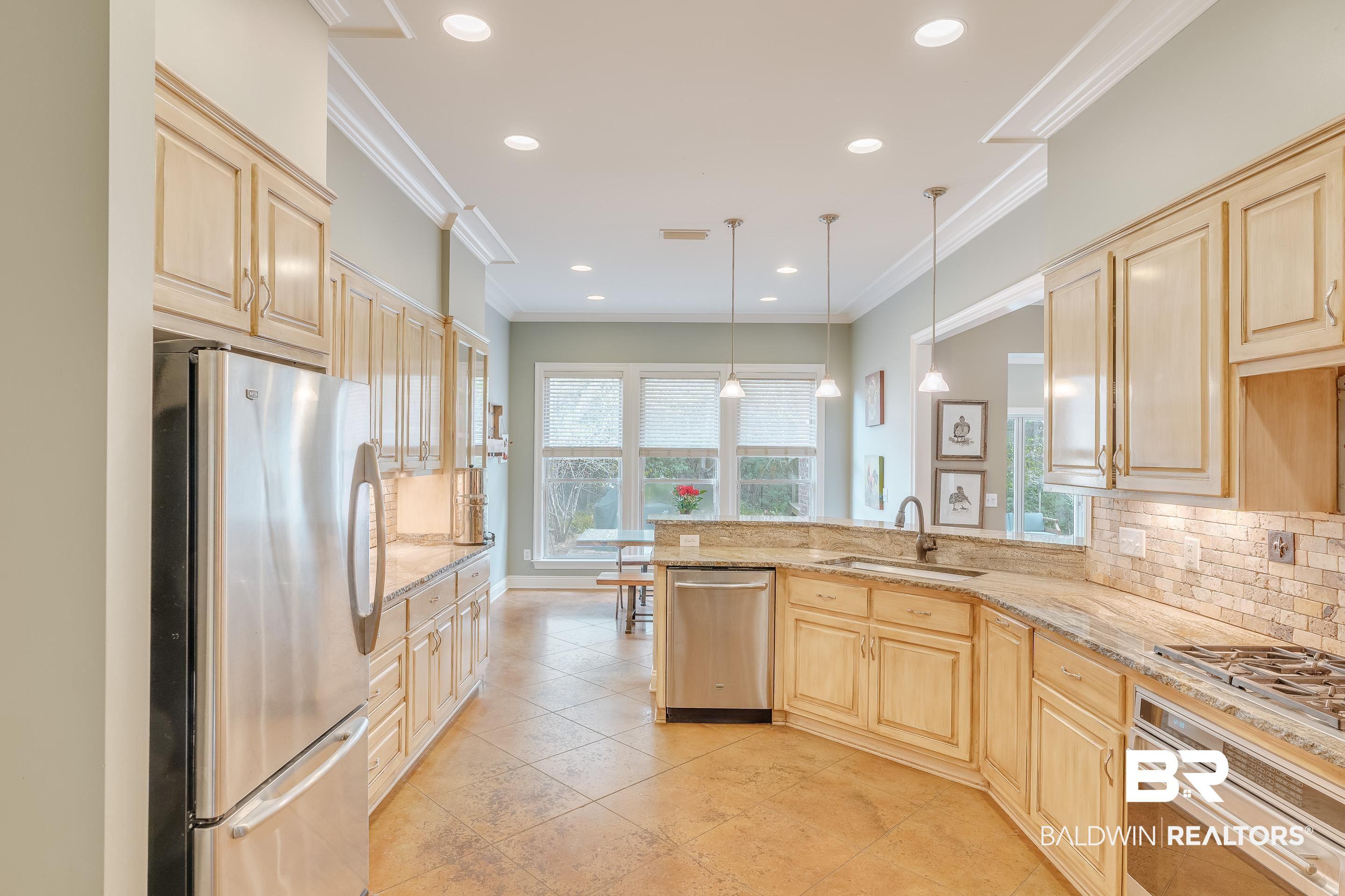 Image 3: Kitchen featuring light wood finish cabinetry, stainless steel appliances, light stone countertops, decorative light fixtures, and a peninsula