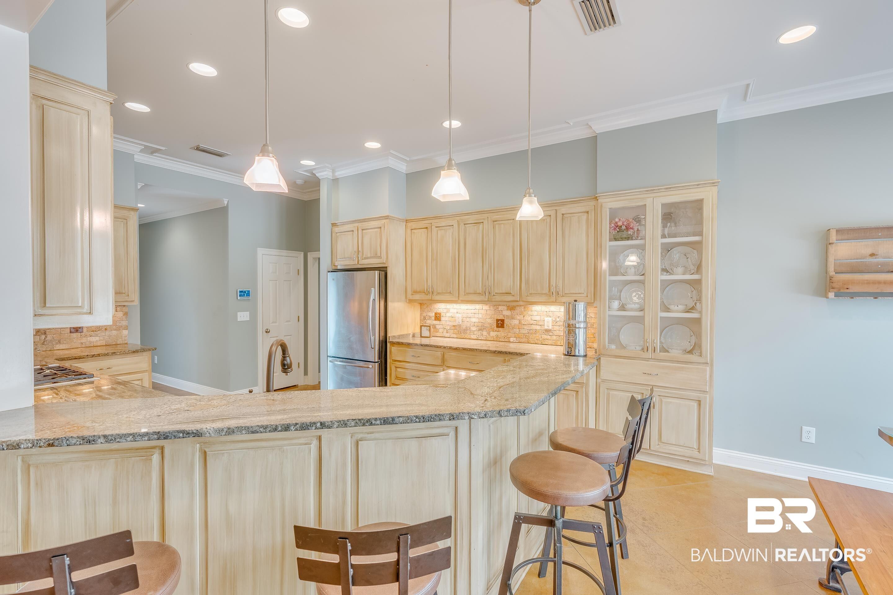 Image 4: Kitchen featuring decorative backsplash, light stone counters, a kitchen breakfast bar, glass fronted cabinets, and ornamental molding