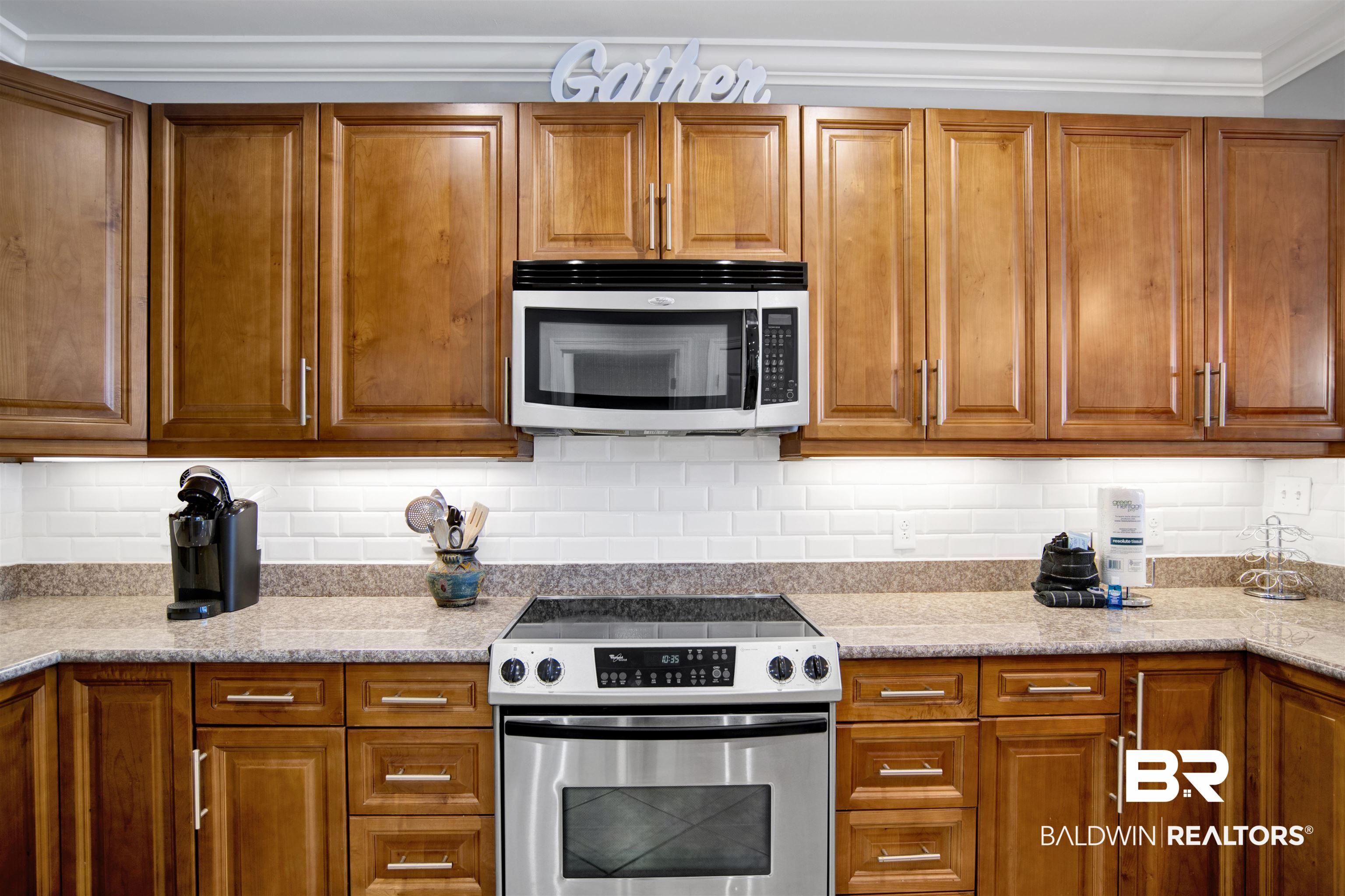 Image 4: Kitchen featuring light wood cabinetry, stone-finish countertops, stainless steel appliances, and a subway tile backsplash