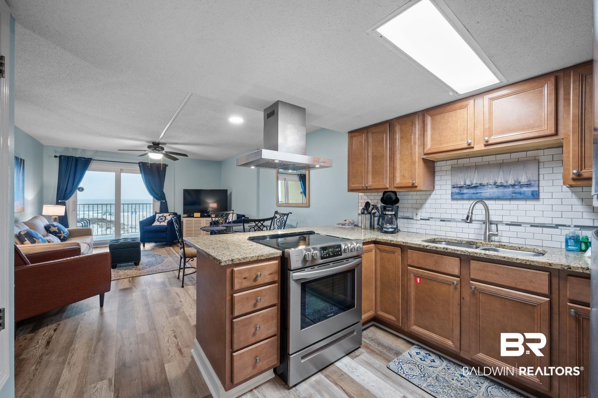 Image 4: Kitchen with brown cabinetry, a peninsula, a sink, stainless steel range with electric cooktop, and exhaust hood