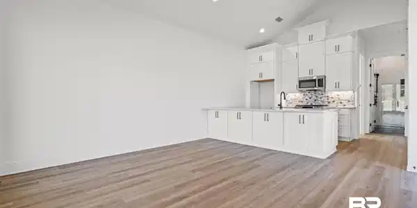 Image 3: Kitchen featuring white cabinetry, open floor plan, light wood-style flooring, tasteful backsplash, and high vaulted ceiling