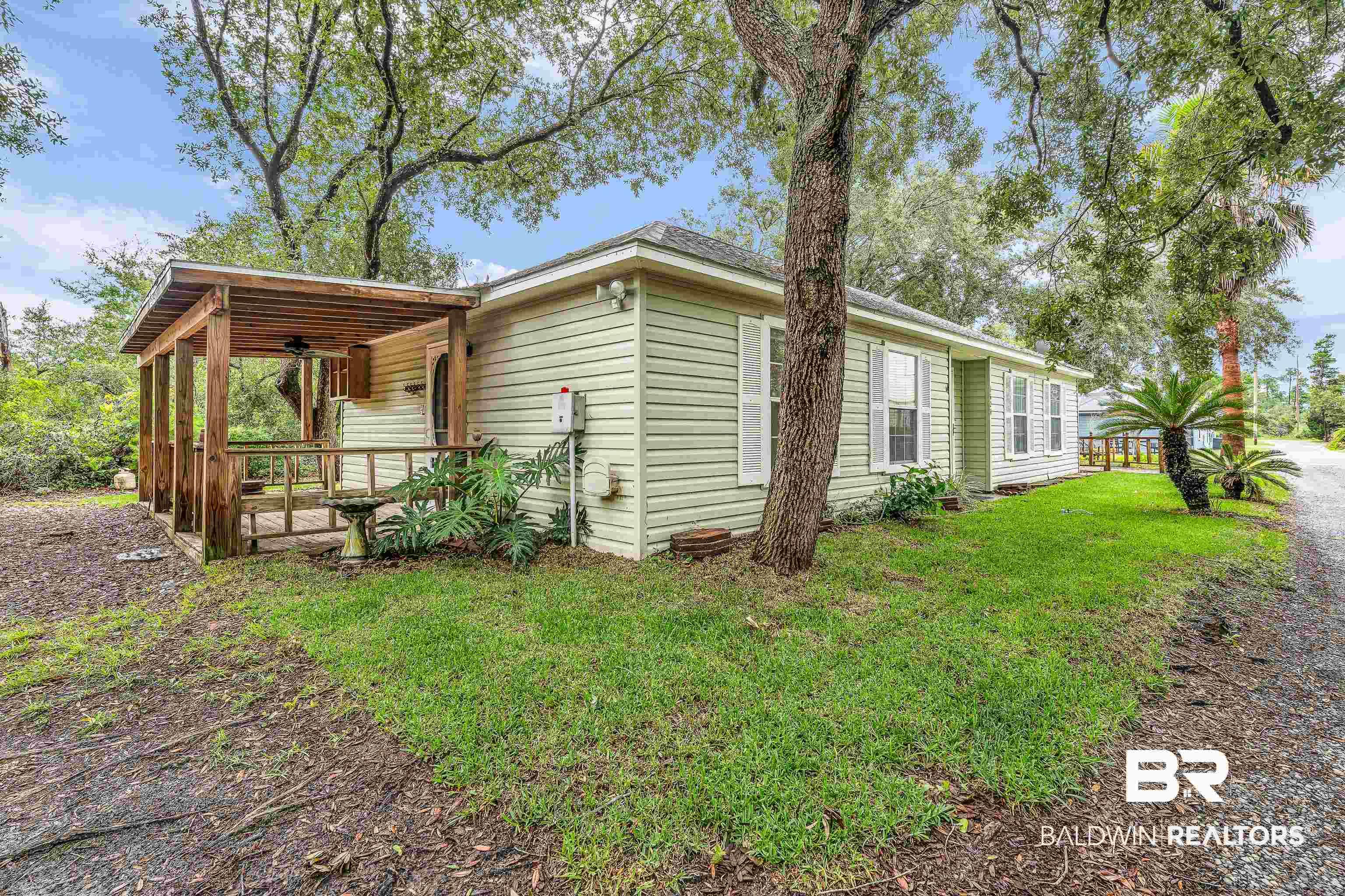 Image 2: Cream-colored siding exterior featuring white window shutters, a covered wood deck, and mature trees