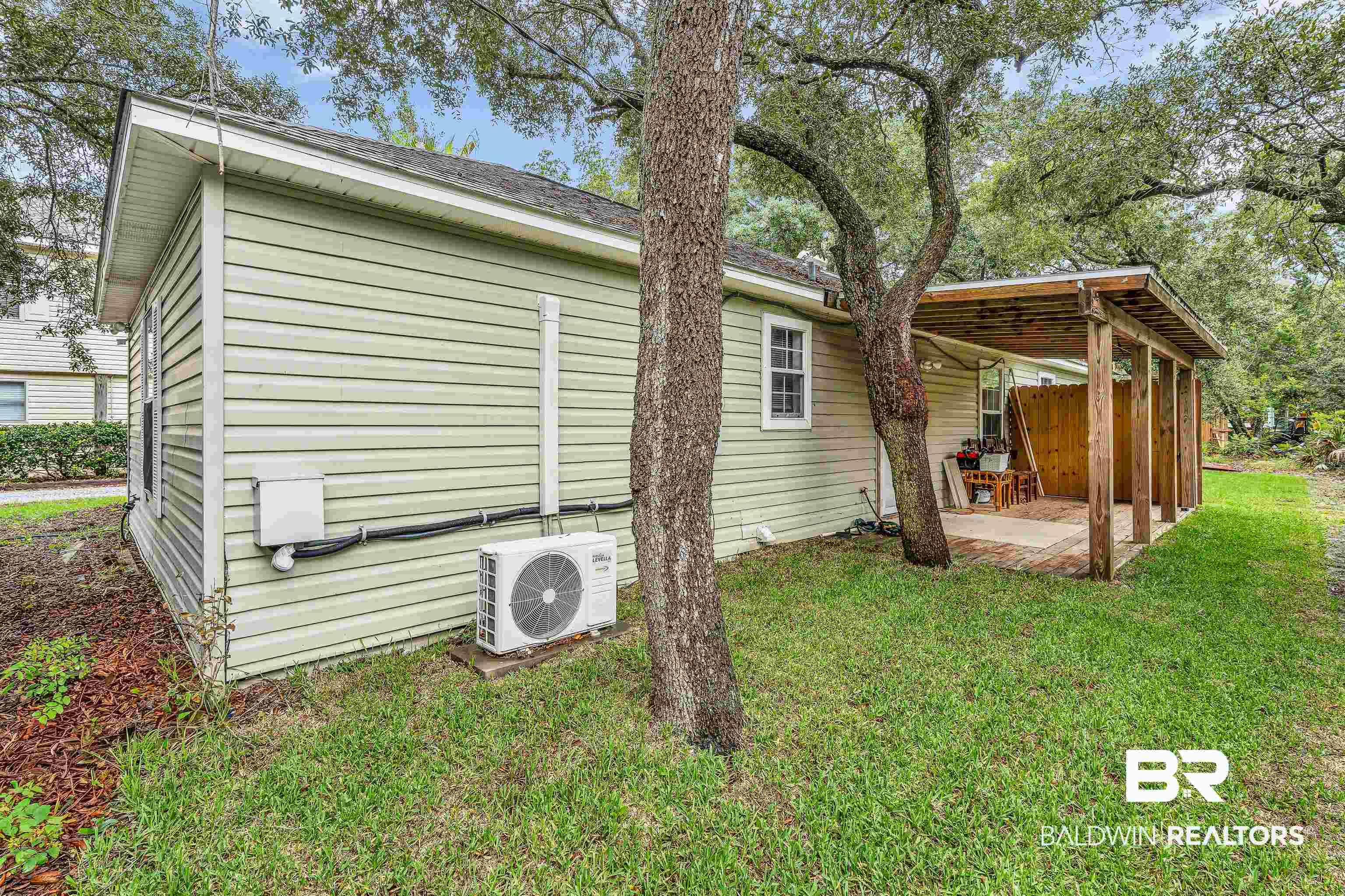 Image 4: Green siding exterior with a covered patio featuring a wood-frame structure and concrete flooring