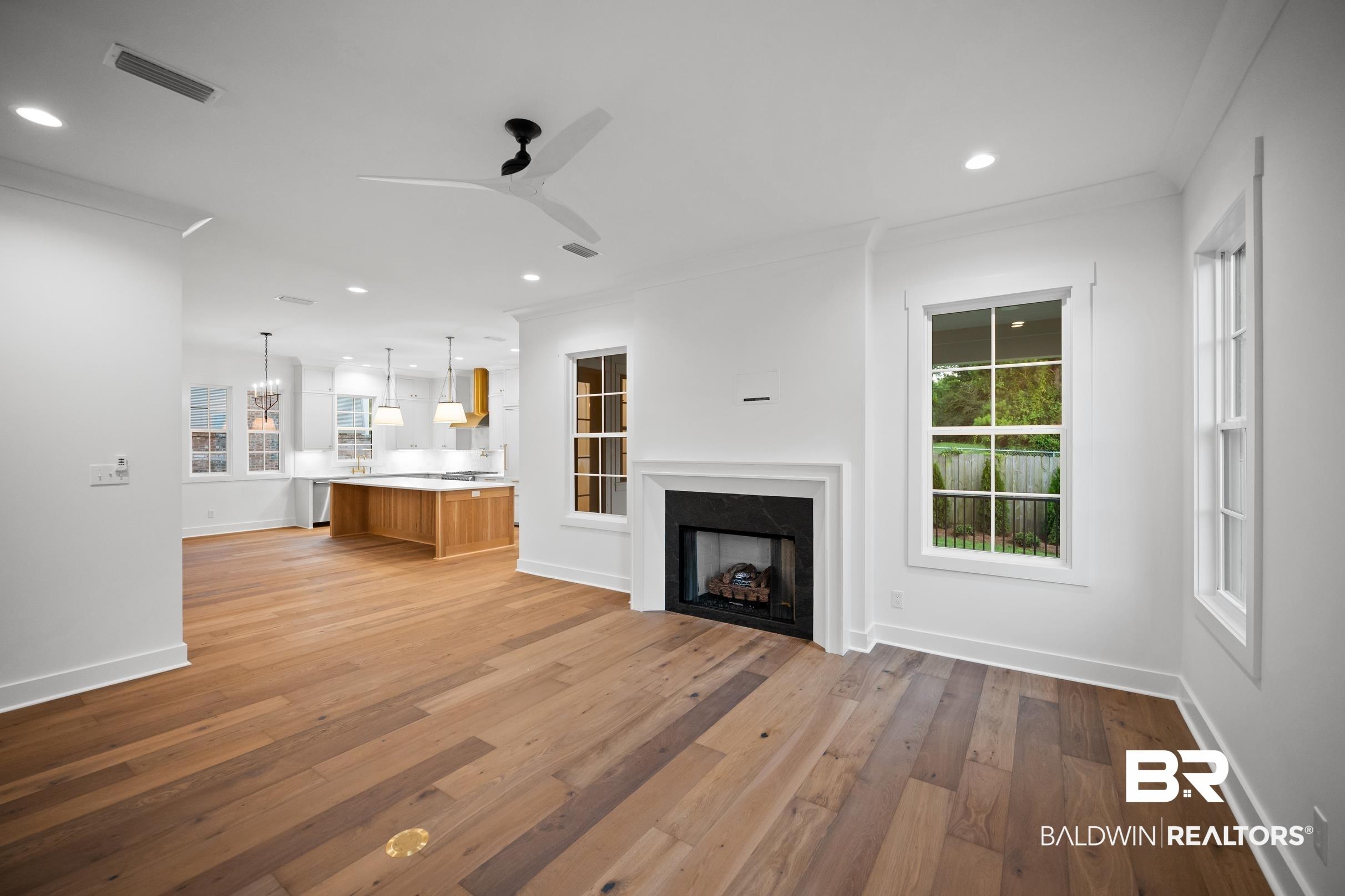 Image 4: Open-concept living area with wood-finish flooring, a contemporary fireplace with a white surround, recessed lighting, and a modern ceiling fan