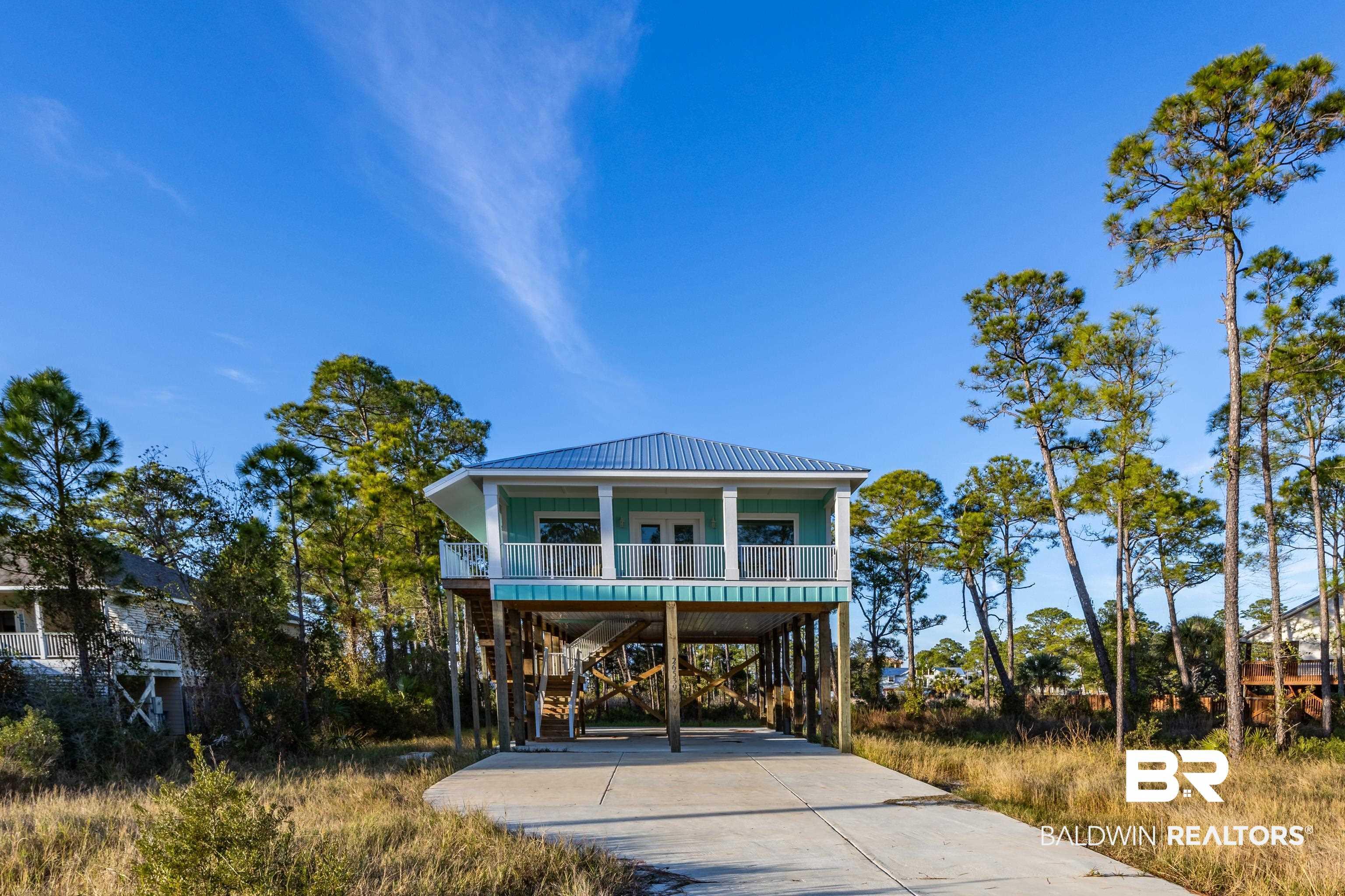 Image 1: Beach home featuring a metal roof, a carport, concrete driveway, stairs, and a porch