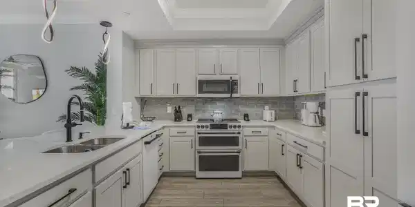 Image 4: Kitchen with stainless steel appliances, light stone countertops, crown molding, pendant lighting, and white cabinetry