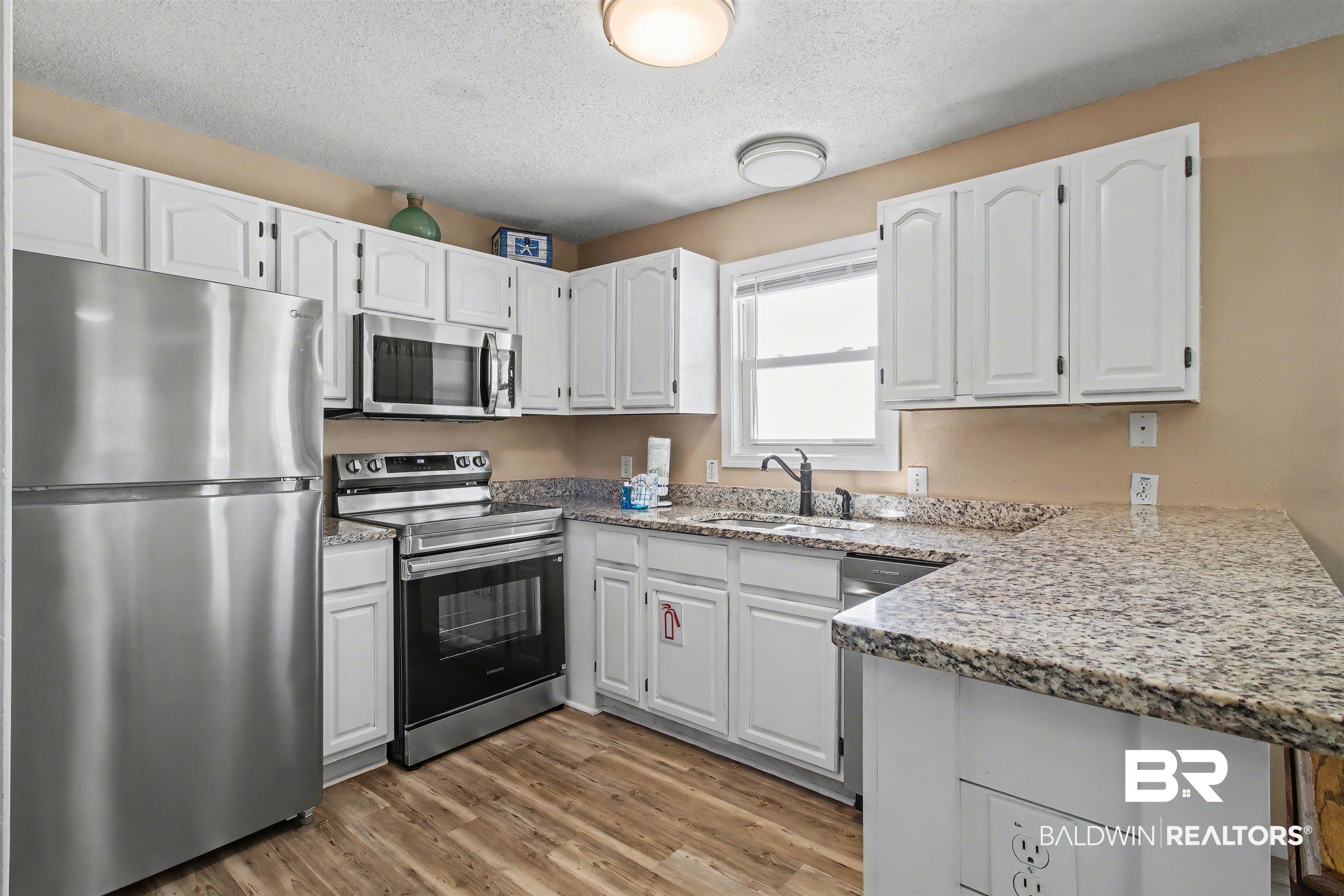 Image 3: Kitchen featuring stainless steel appliances, white cabinetry, light stone countertops, a peninsula, and light wood-style floors