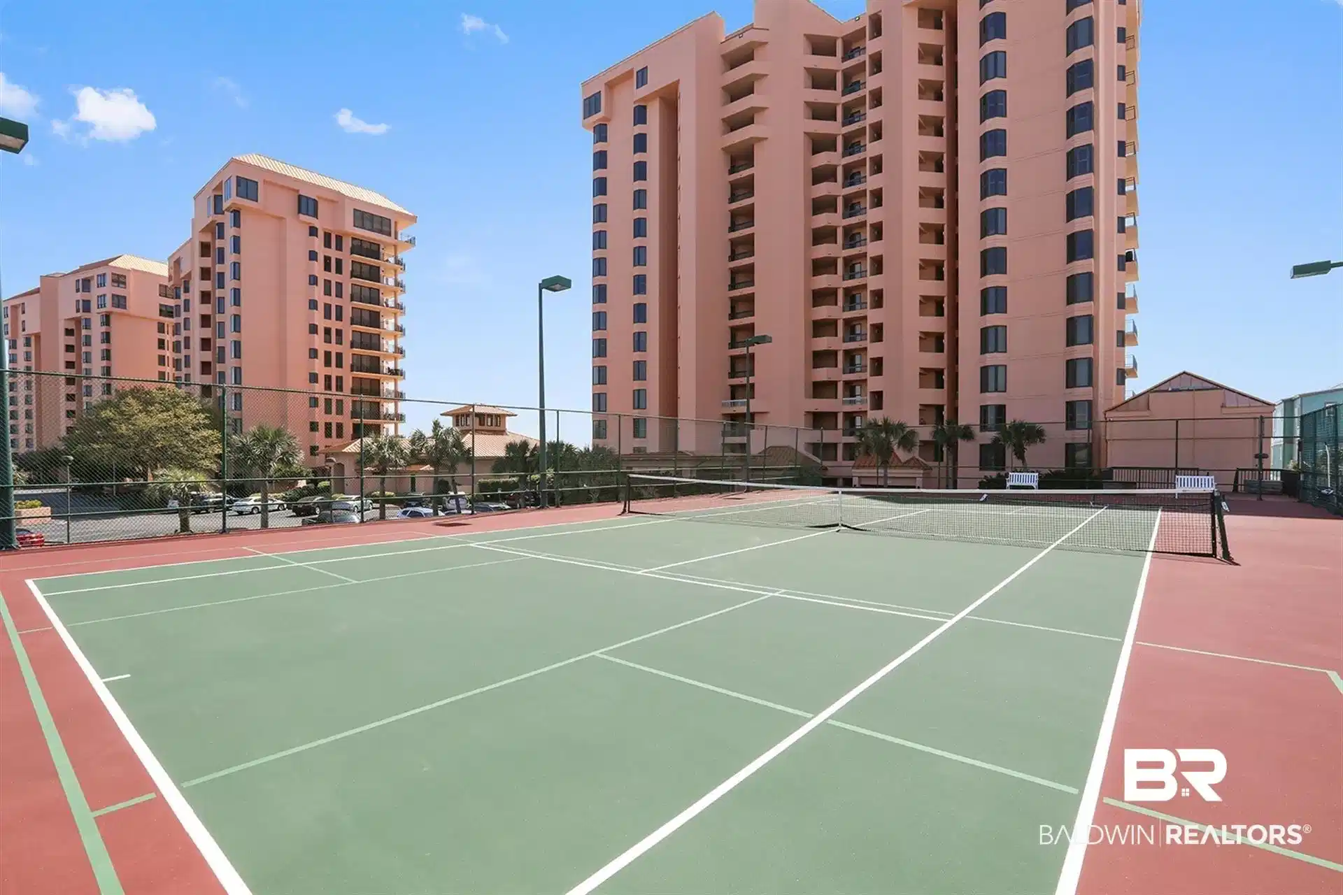 Image 1: Outdoor tennis court featuring a green playing surface and red perimeter