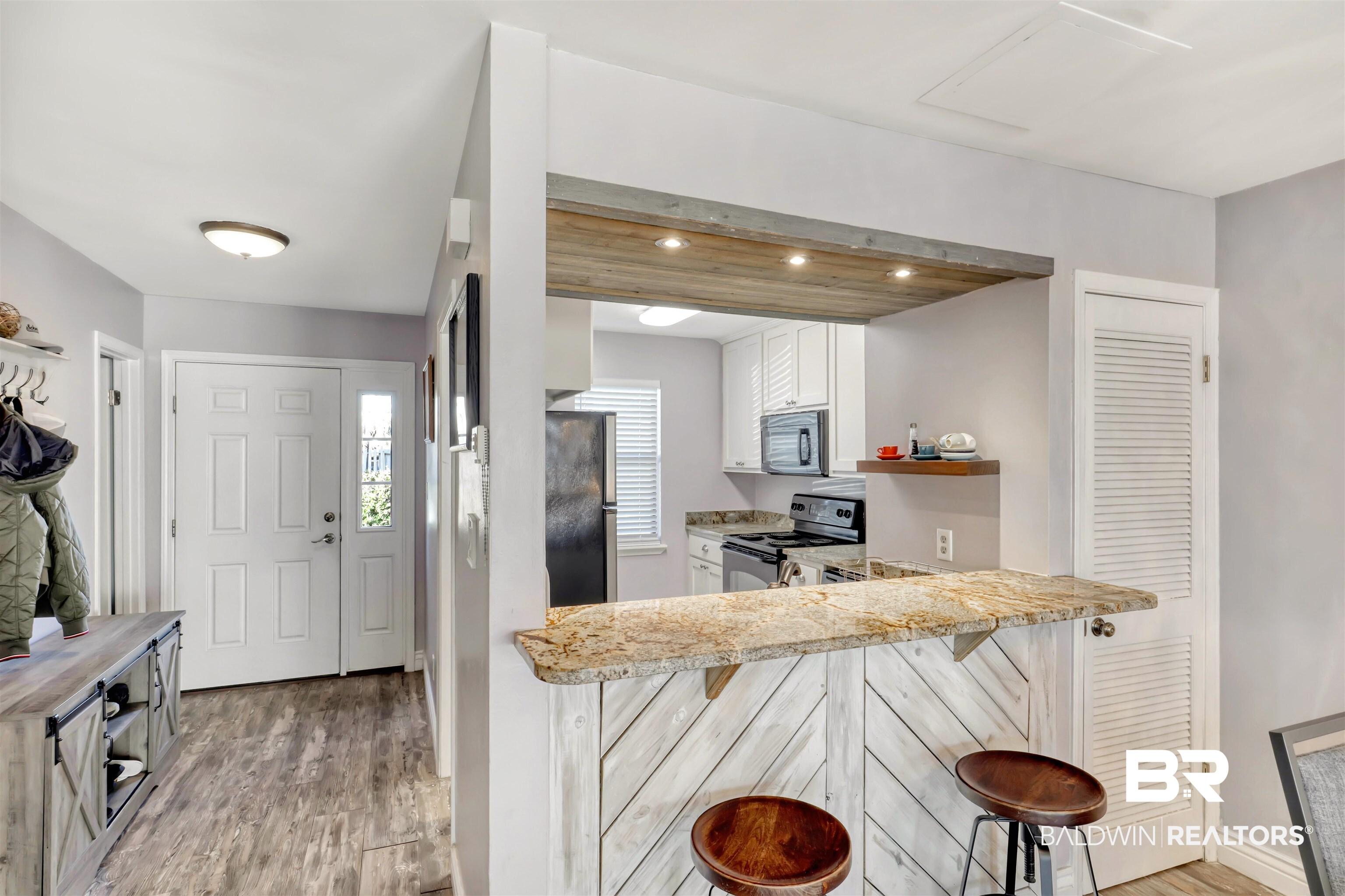 Image 2: Kitchen with a breakfast bar, open shelves, light wood finished floors, black appliances, and recessed lighting