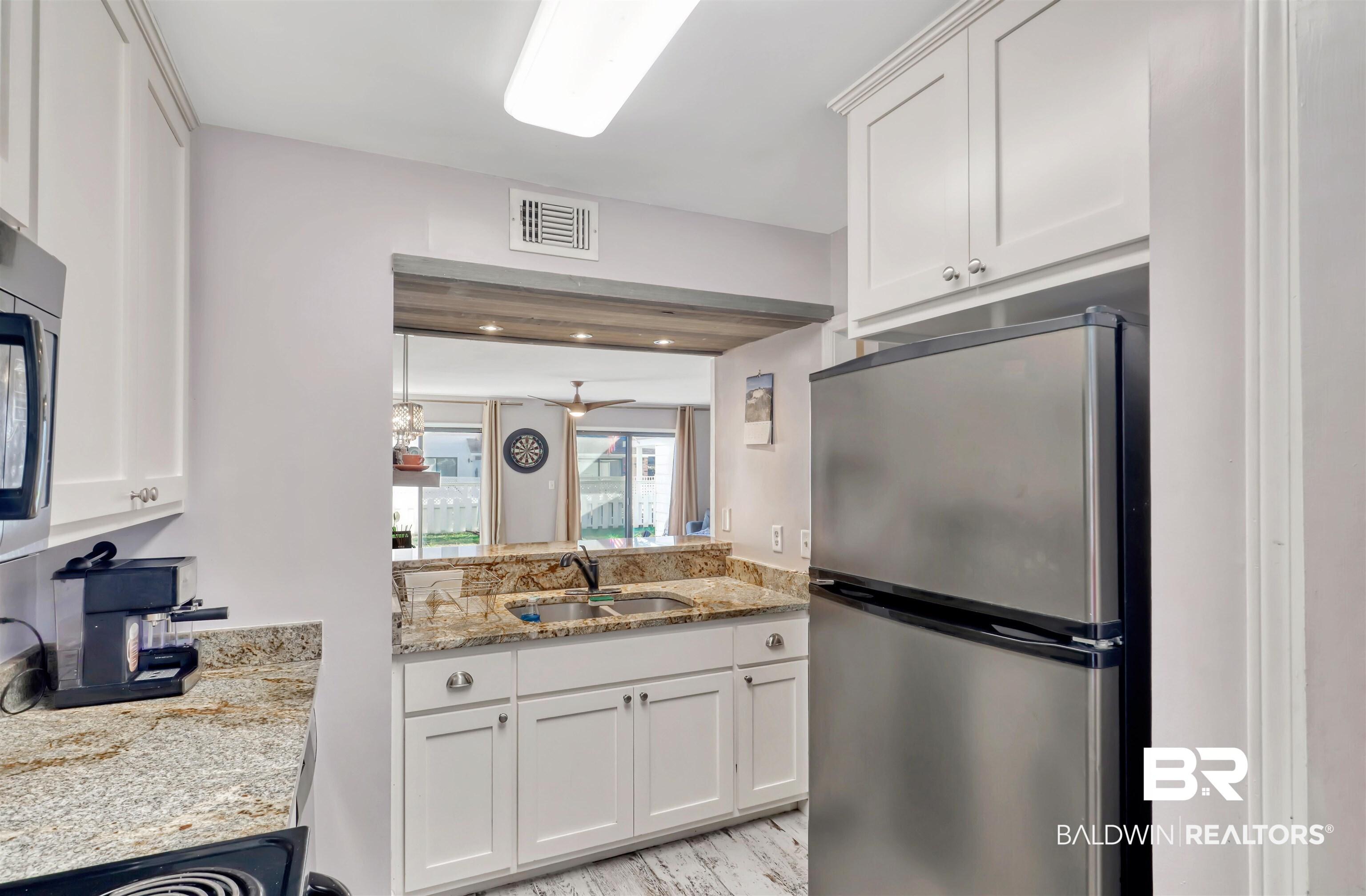Image 3: Kitchen featuring stainless steel appliances, light stone counters, and white cabinetry