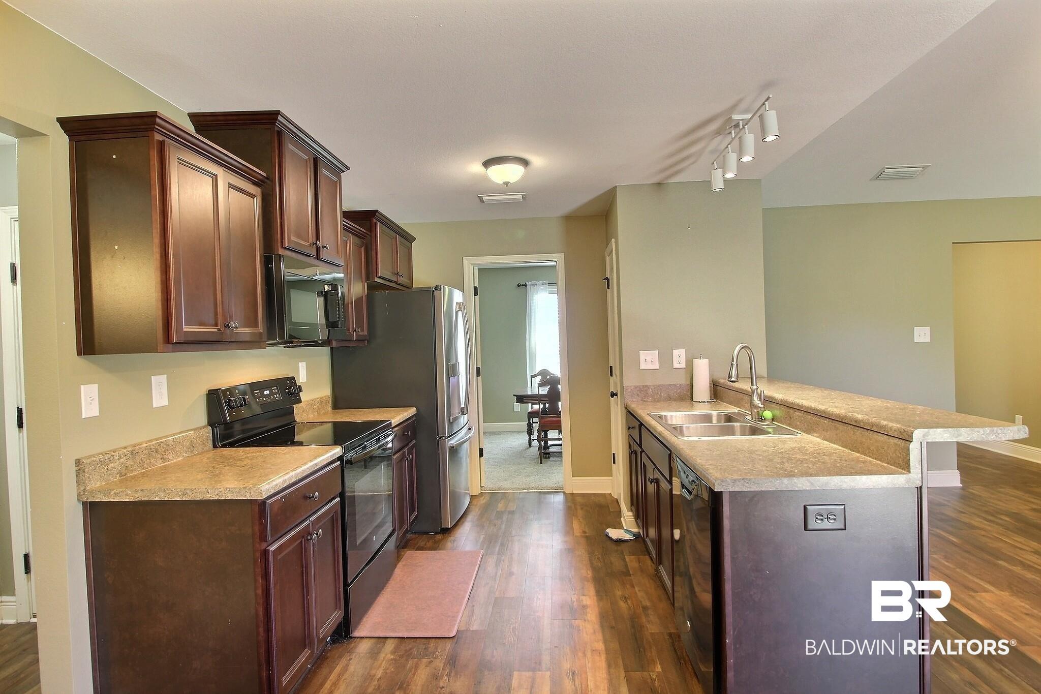 Image 4: Kitchen with black appliances, a peninsula, dark wood-style floors, dark brown cabinets, and light countertops