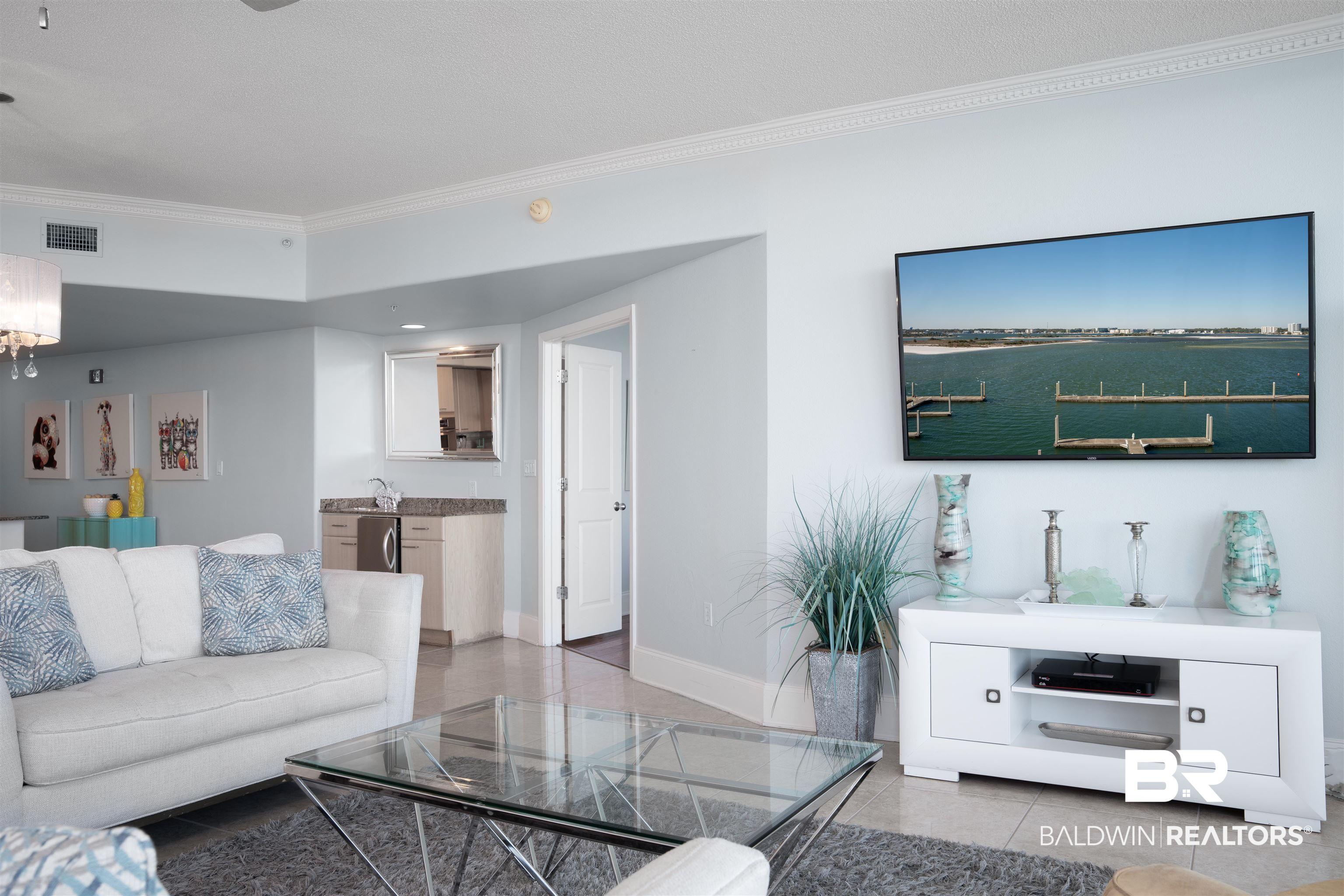 Image 4: Living area featuring light-toned tile flooring, crown molding, and a built-in wet bar with a compact refrigerator and undermount sink