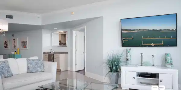 Image 4: Living area featuring light-toned tile flooring, crown molding, and a built-in wet bar with a compact refrigerator and undermount sink