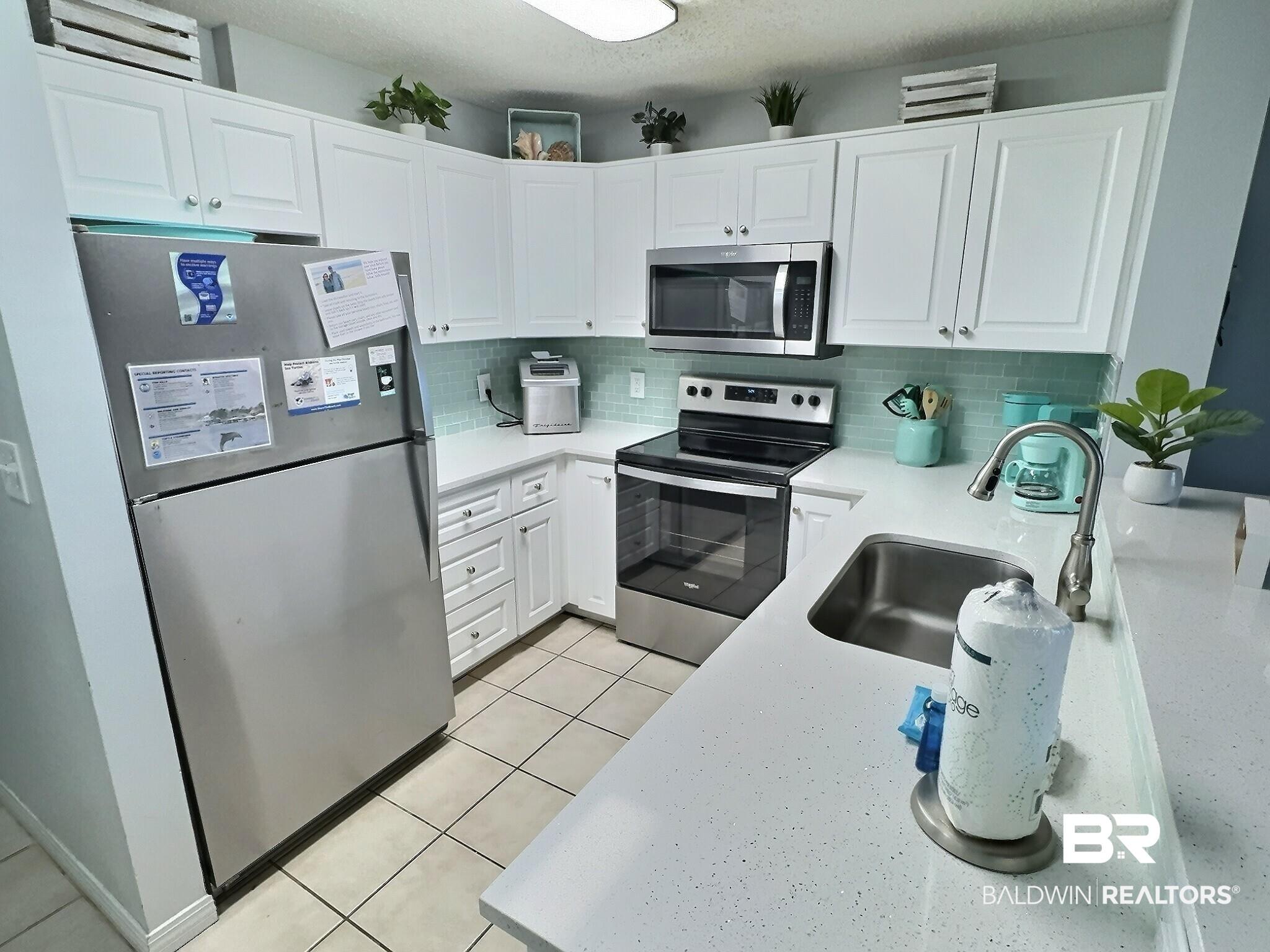 Image 4: Kitchen with stainless steel appliances, white cabinets, tasteful backsplash, light stone counters, and light tile patterned flooring