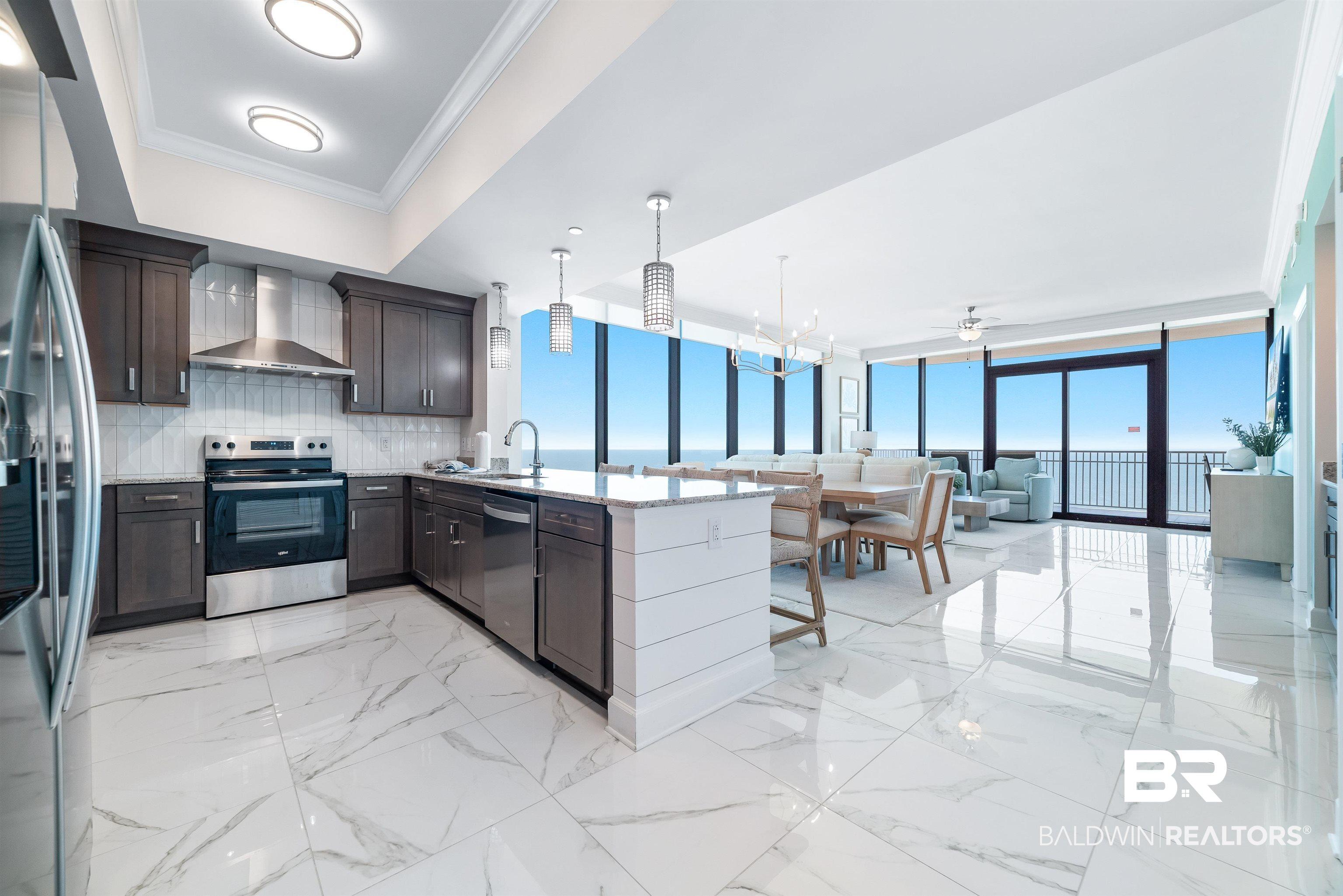 Image 2: Open concept interior featuring large format marble-look tile flooring, floor-to-ceiling windows, stainless steel appliances, dark wood cabinetry, and a shiplap island